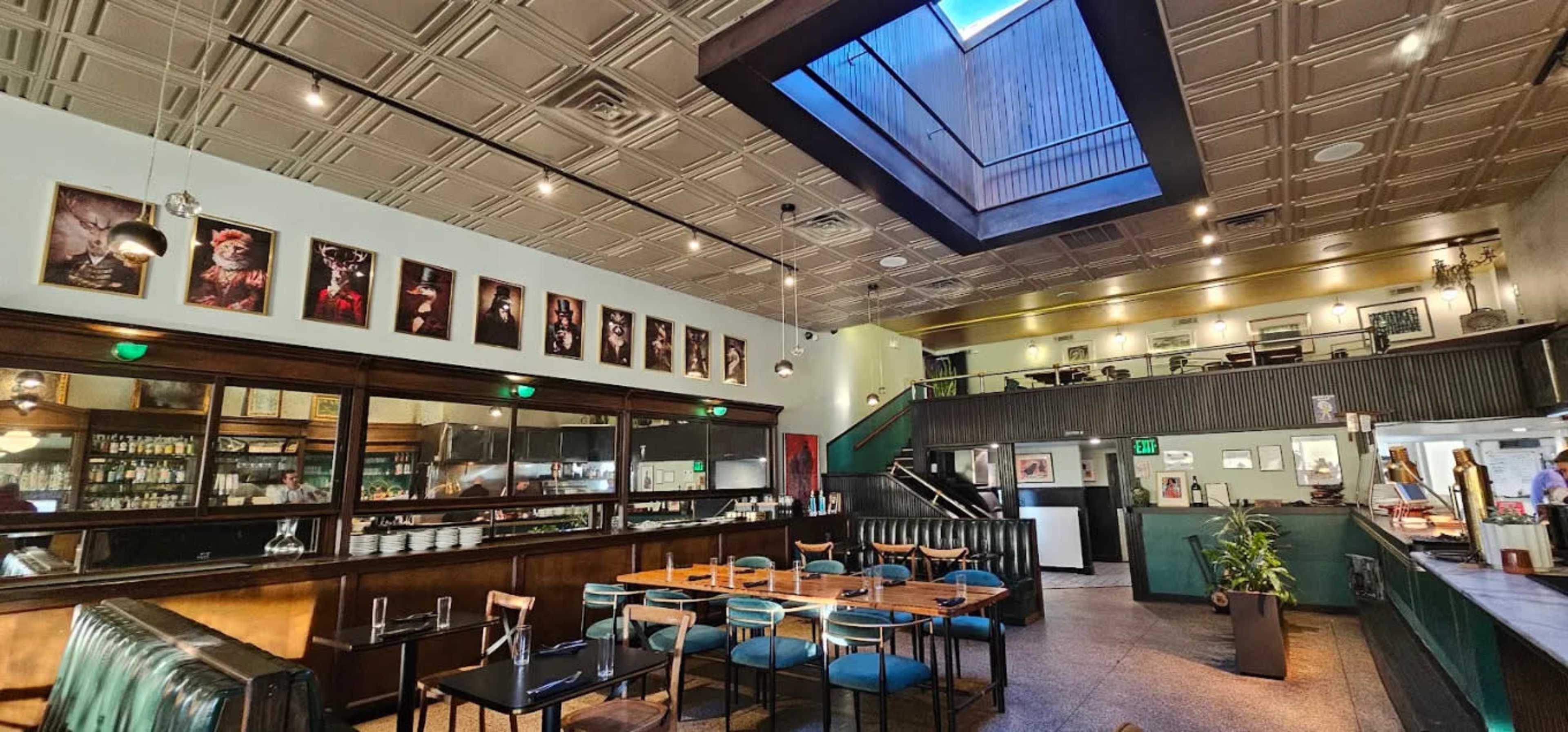 The image shows the interior of a restaurant featuring a high ceiling, a skylight, and a mix of seating arrangements with tables and booth-style seating along one wall.