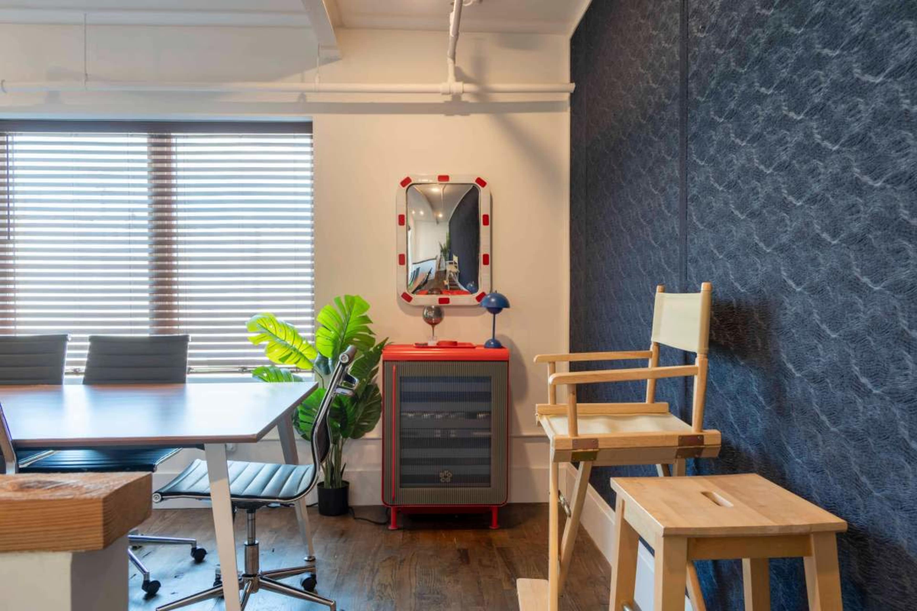 The image shows a modern office meeting room with a table, chairs, a decorative plant, and vintage-style furniture including an illuminated mirror and a wooden stool.