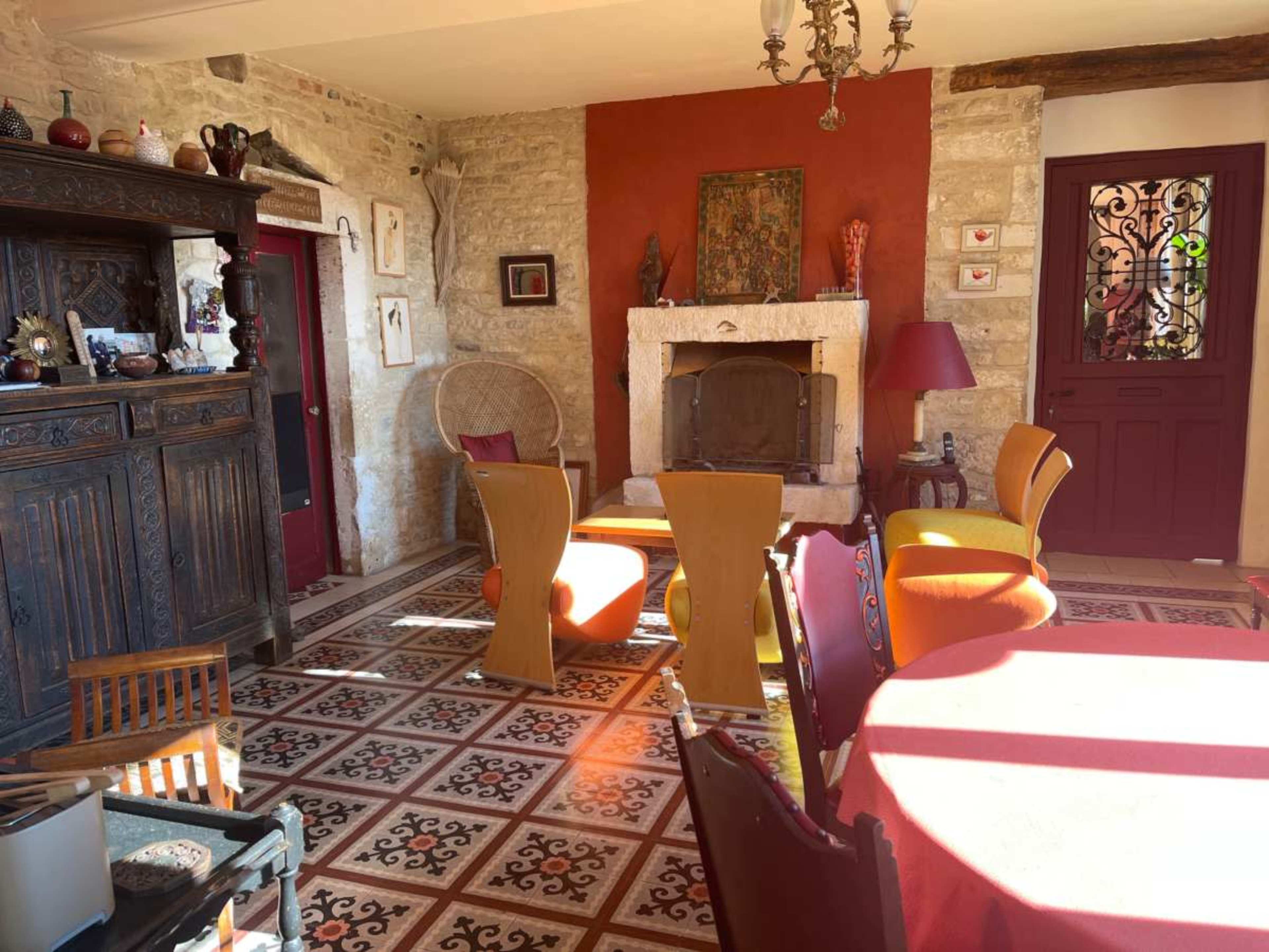 The image shows a cozy living room with a stone fireplace, a decorative wooden cabinet, colorful furniture, and patterned tile flooring.
