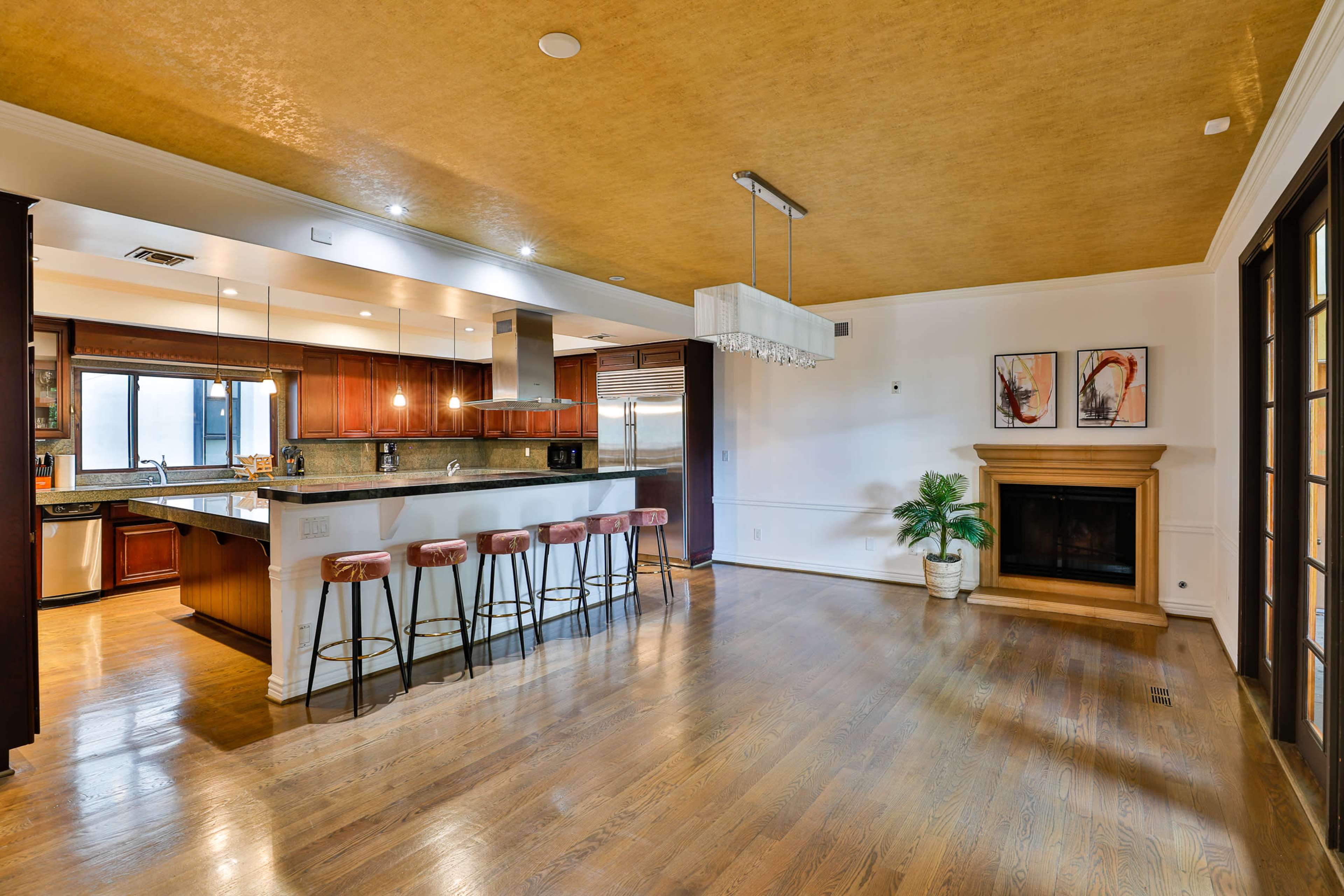 A spacious kitchen and dining area with a fireplace, hardwood flooring, and a bar with four stools.