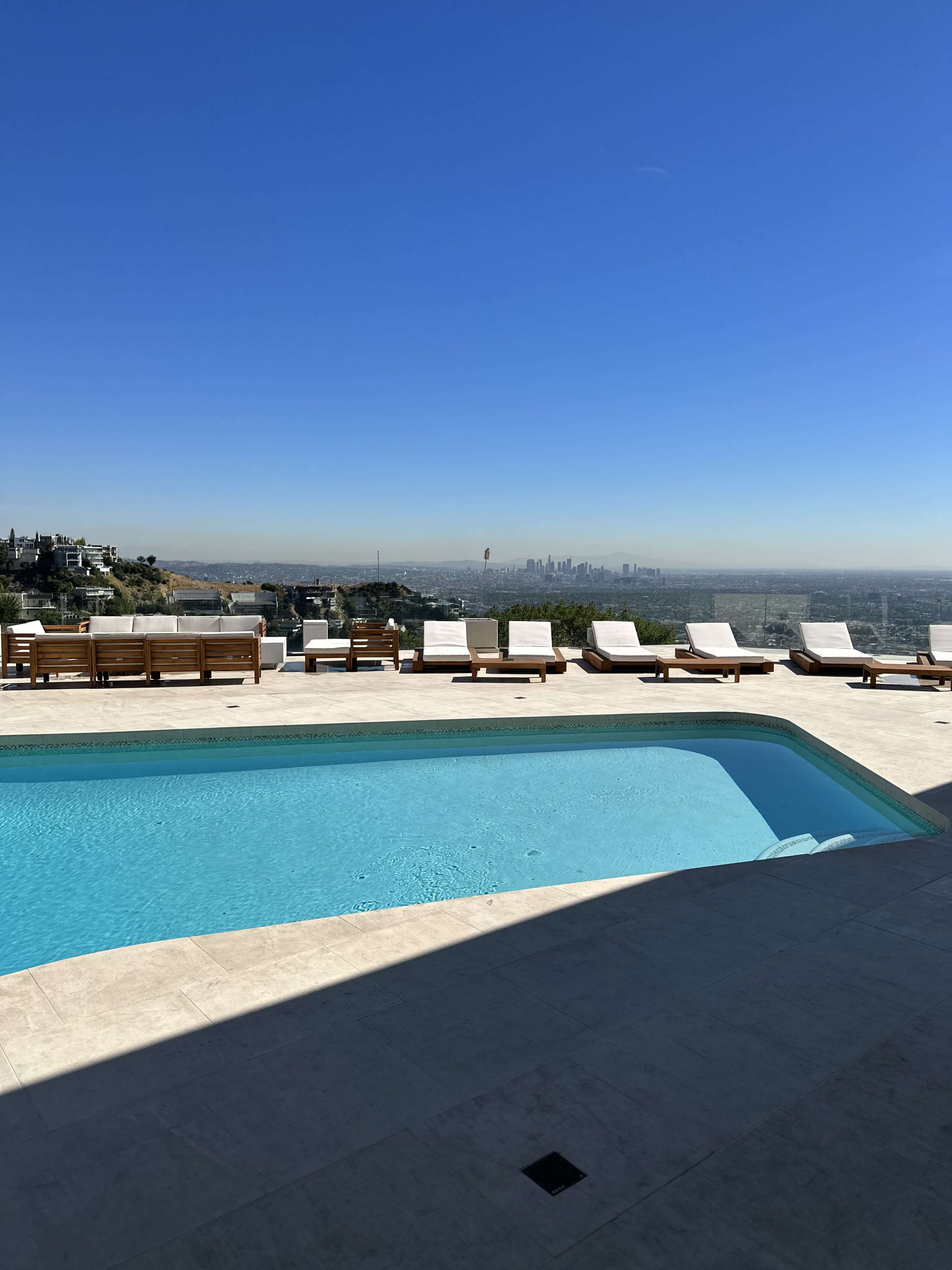 A swimming pool with lounge chairs overlooks a city skyline under a clear blue sky.