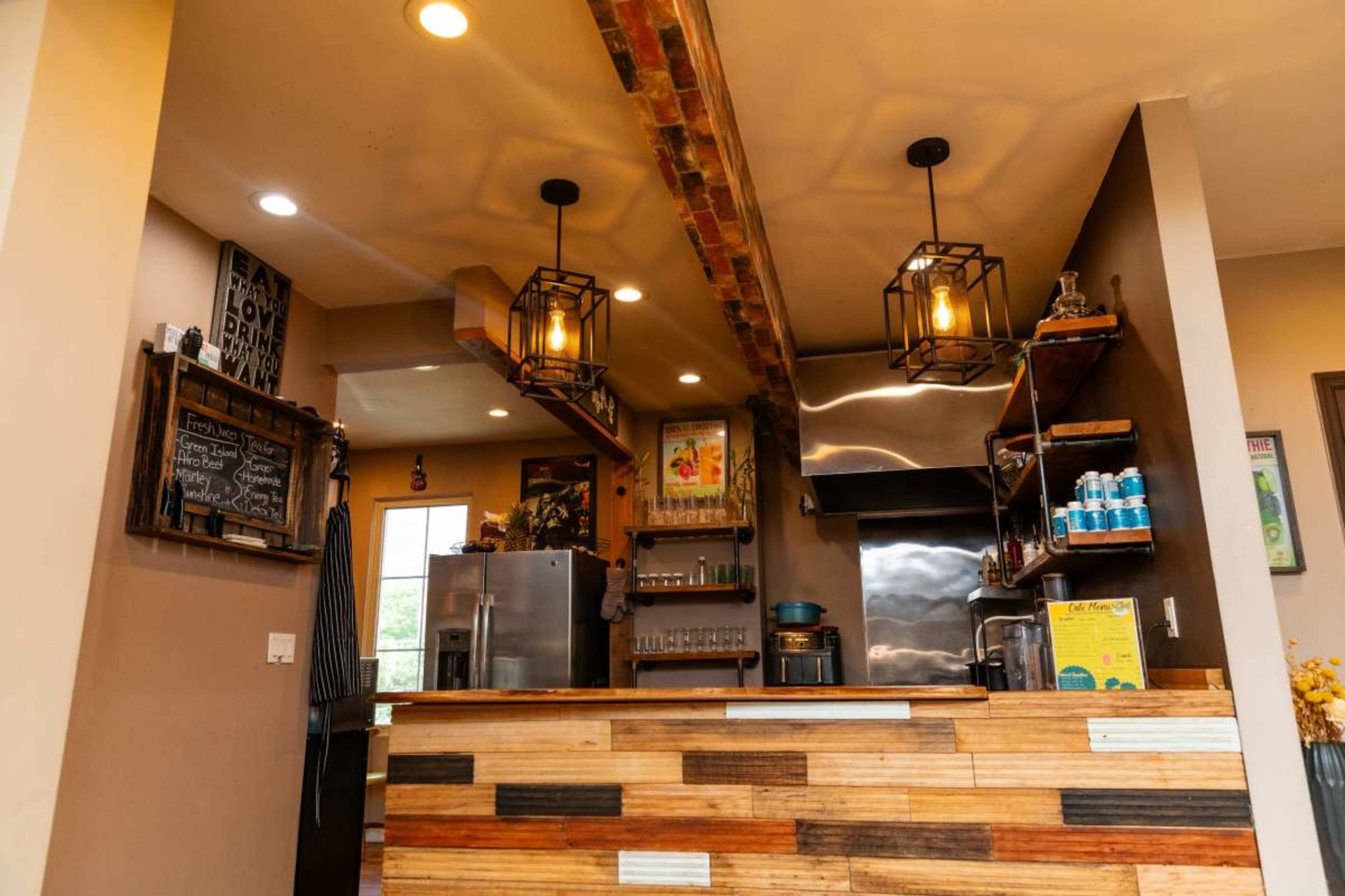 The image shows a rustic café interior featuring a wooden counter, open shelving, and industrial-style light fixtures.