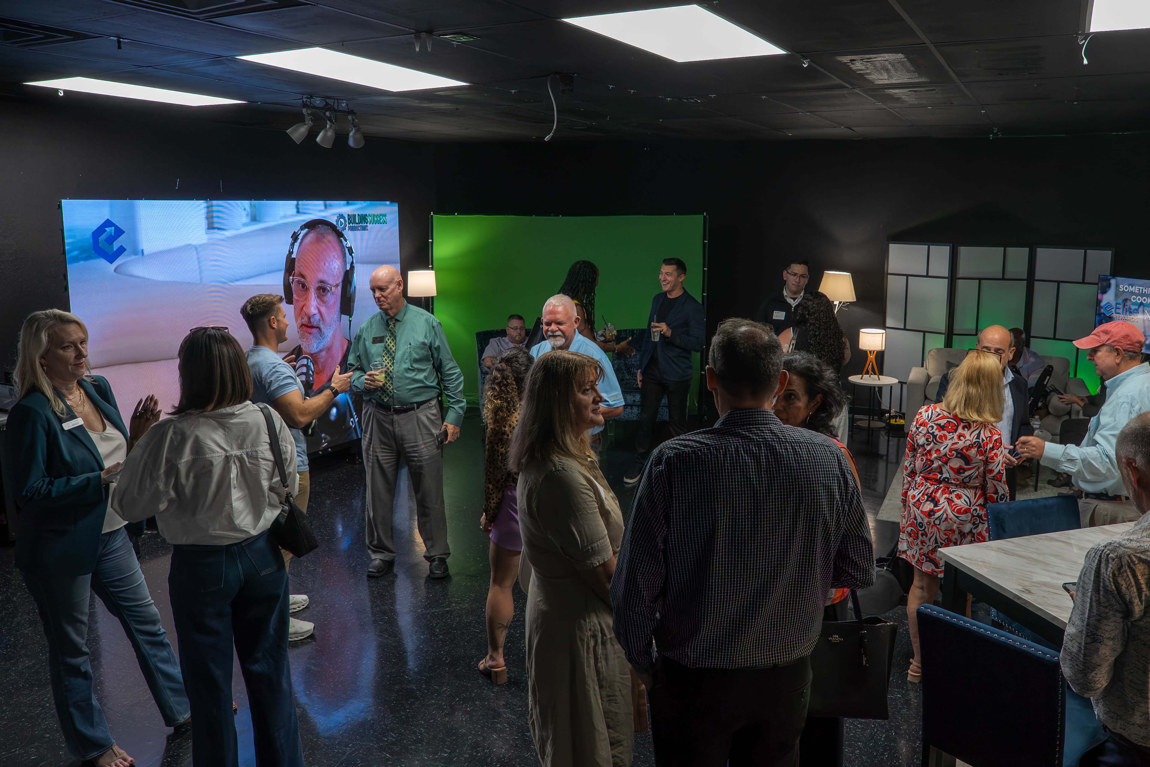 A group of people engage in conversation in a studio space with green and blue screens and various lighting setups.