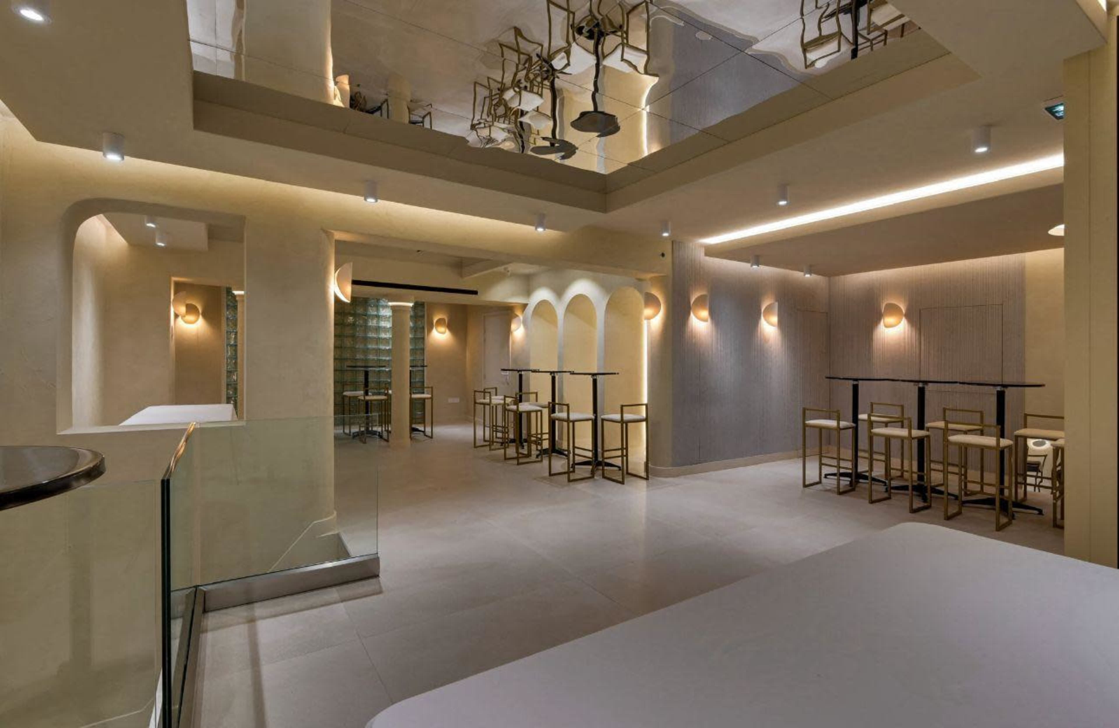 The image shows a modern, minimalistic interior of a restaurant or café featuring tables and chairs, soft lighting, and architectural arches.