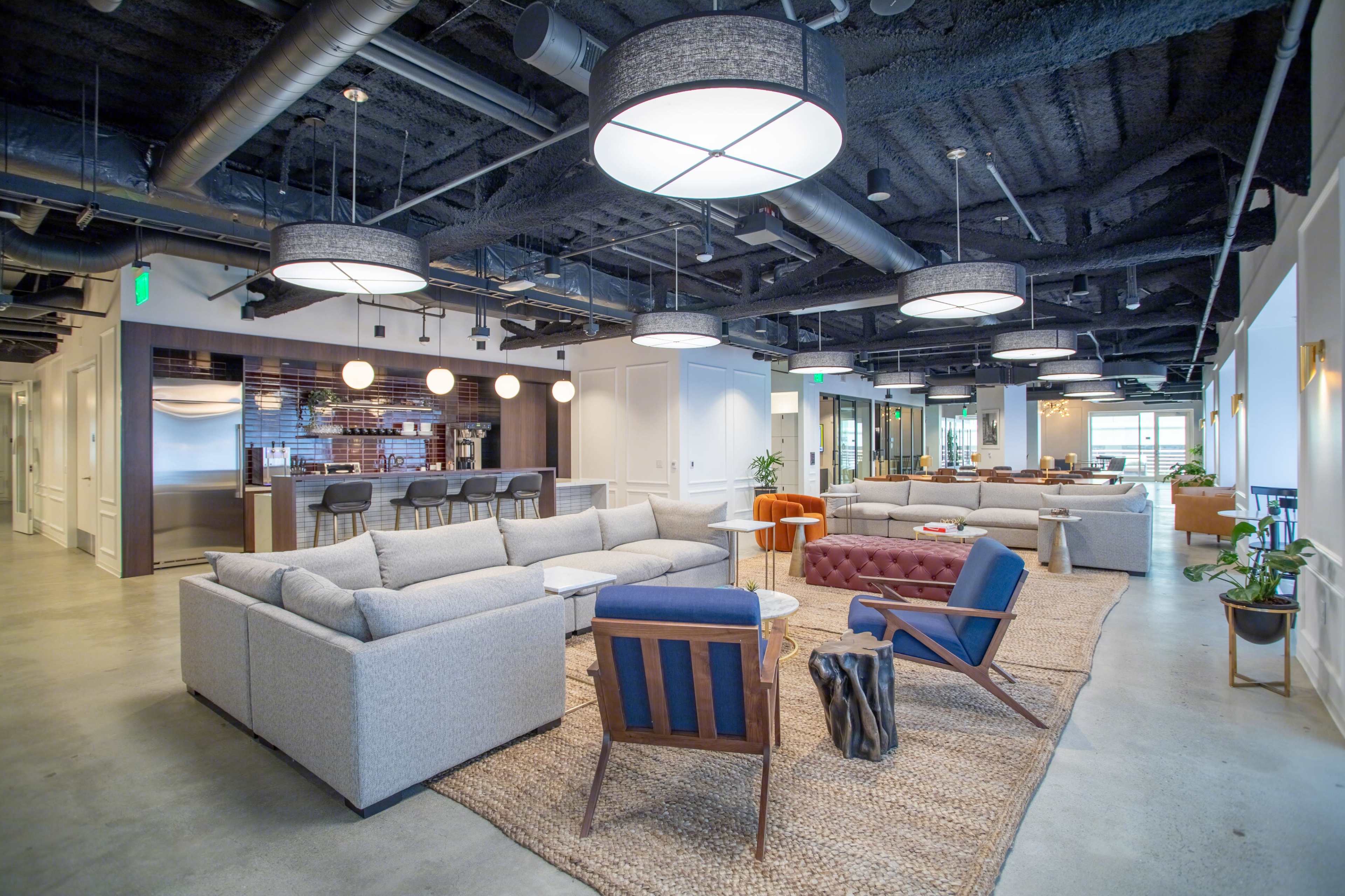 A modern office lounge area with gray sofas, a brown tufted chair, and round pendant lights hanging from the ceiling.