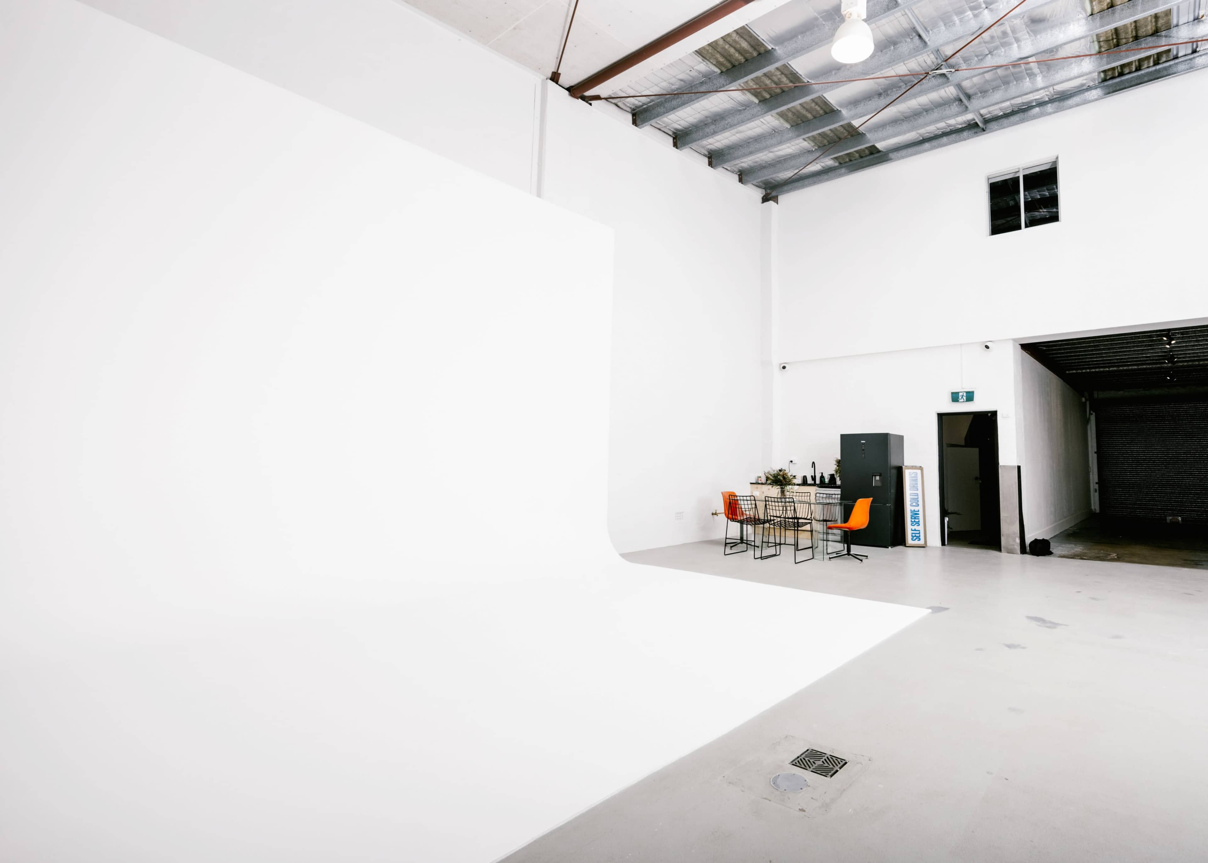 A spacious studio with a large white backdrop, a table set with chairs, and storage cabinets against the walls.