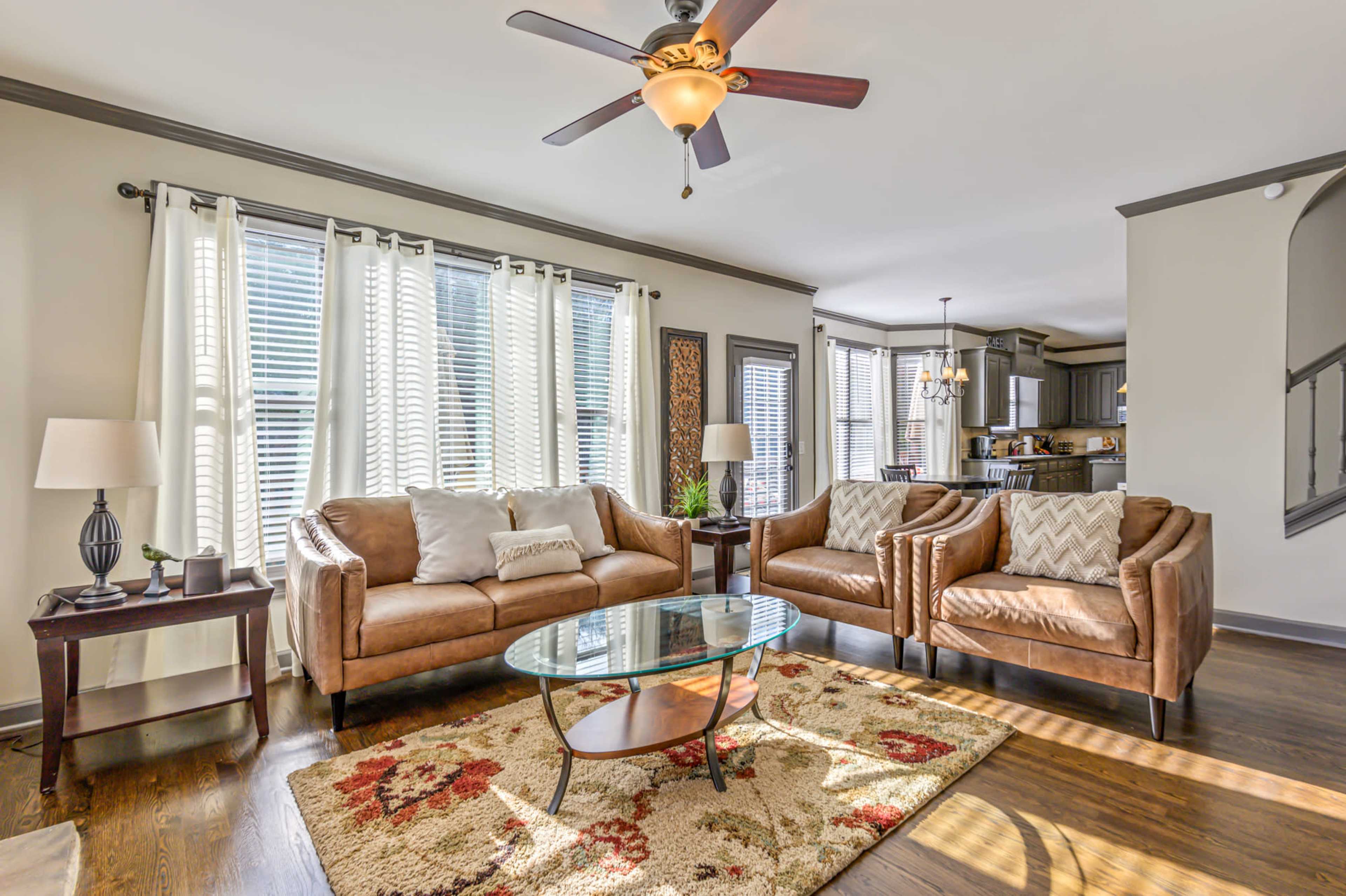 A living room features brown leather sofas, a glass coffee table, and large windows with sheer curtains.