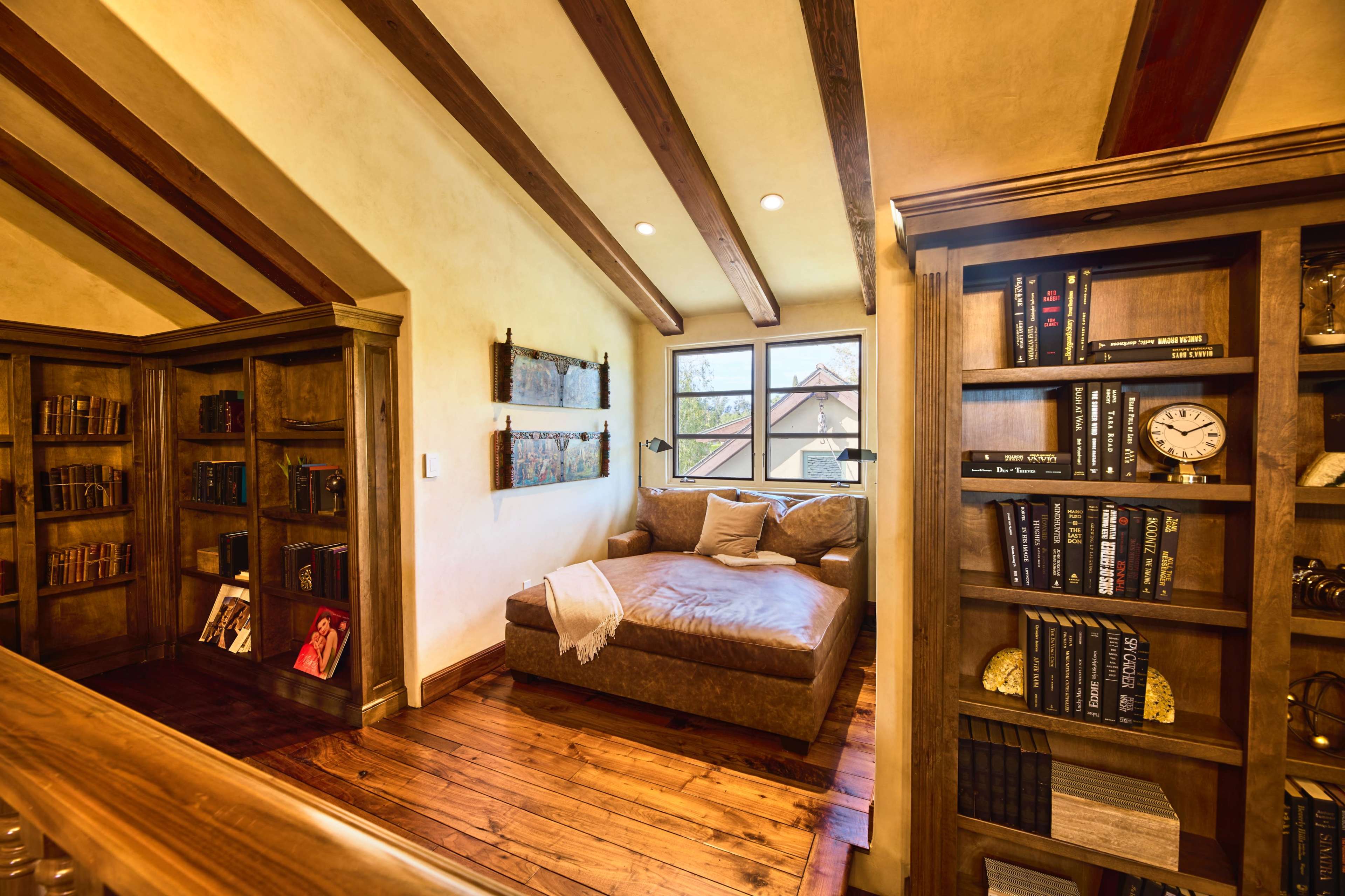 A cozy reading nook with a brown chaise lounge positioned near a window, surrounded by wooden bookshelves filled with books.