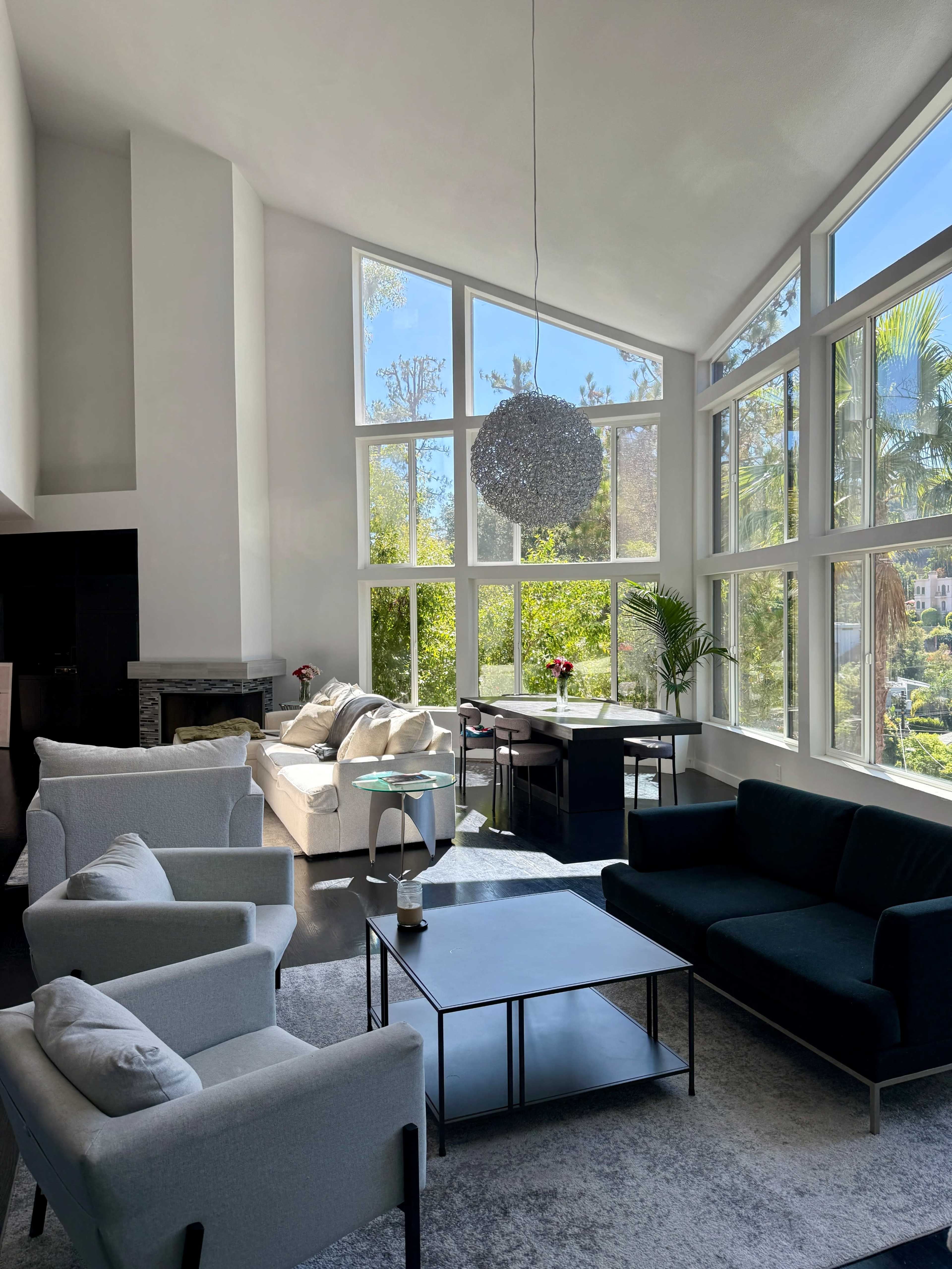 The living room features large windows, white and black furniture, and a modern chandelier, all illuminated by natural light.