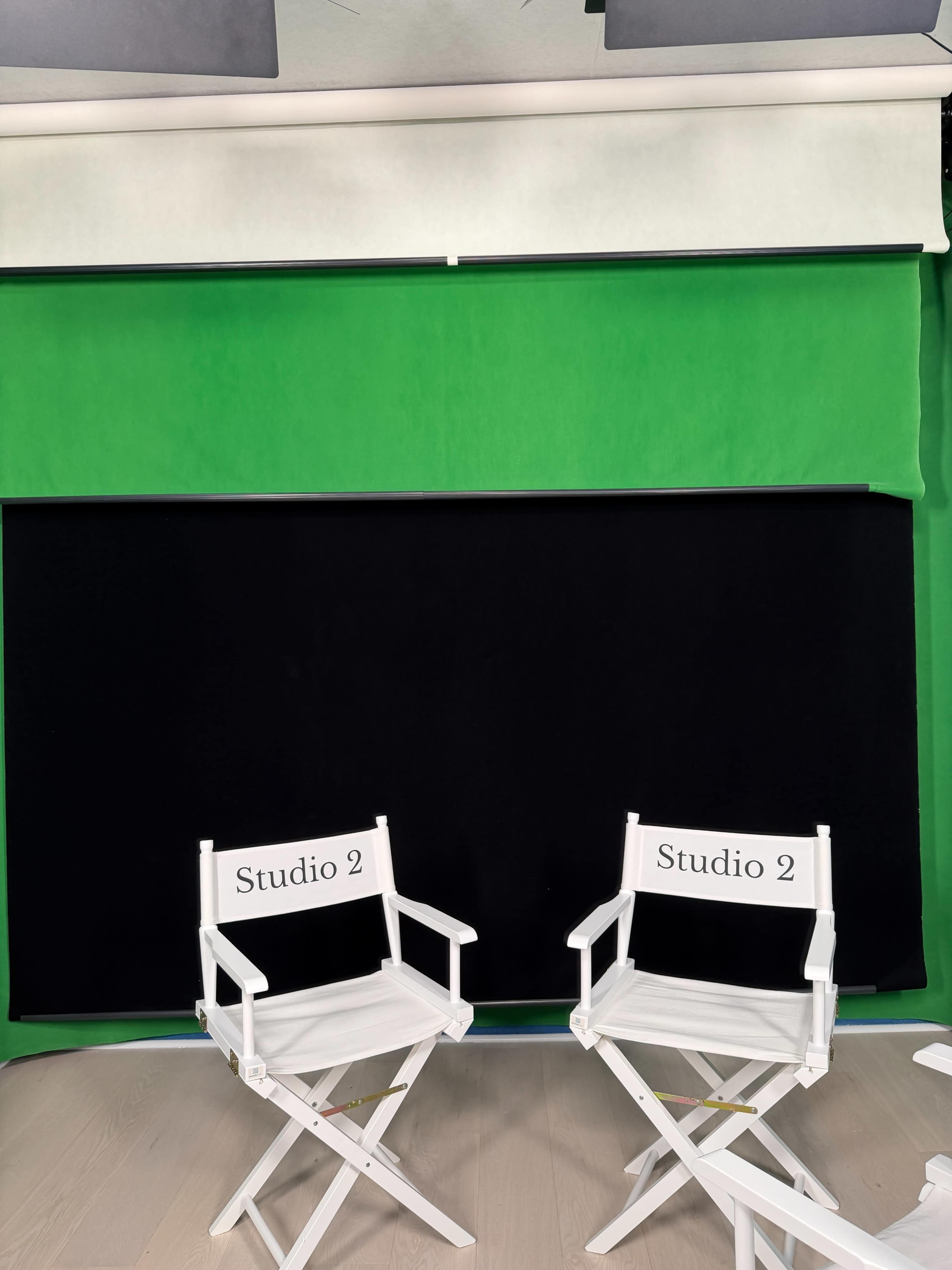 The image shows two white director's chairs labeled "Studio 2" in front of a green screen backdrop and a black panel in a studio setting.