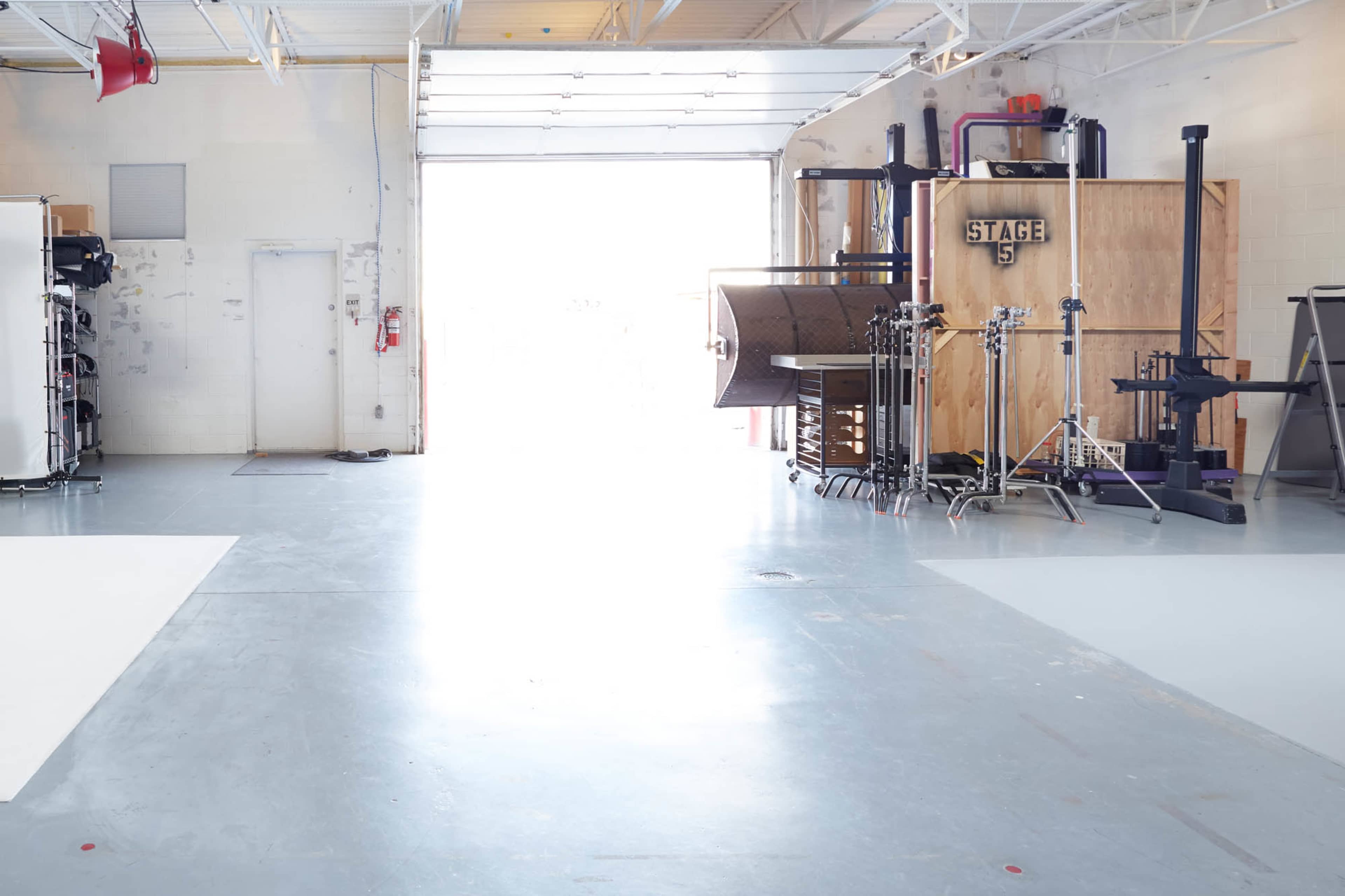 An industrial space features a large open area leading to a bright entrance, with various equipment and a stage setup along the side.