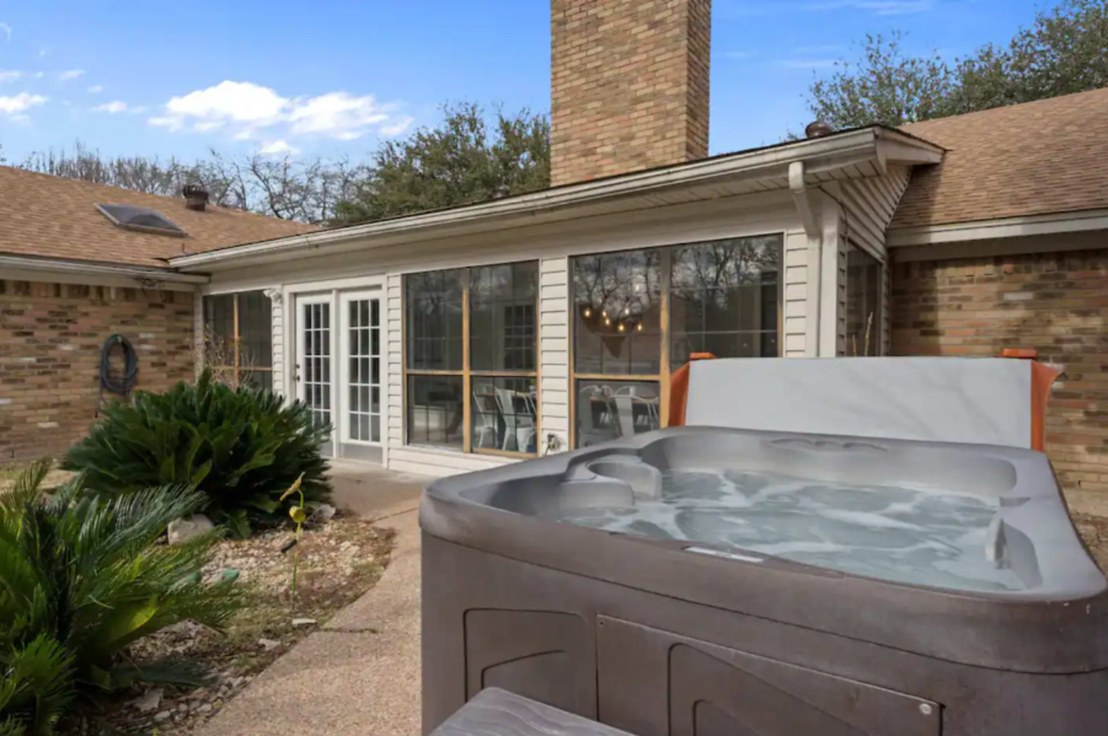 A hot tub sits in the foreground of a patio area adjacent to a house with large glass doors and a brick exterior.