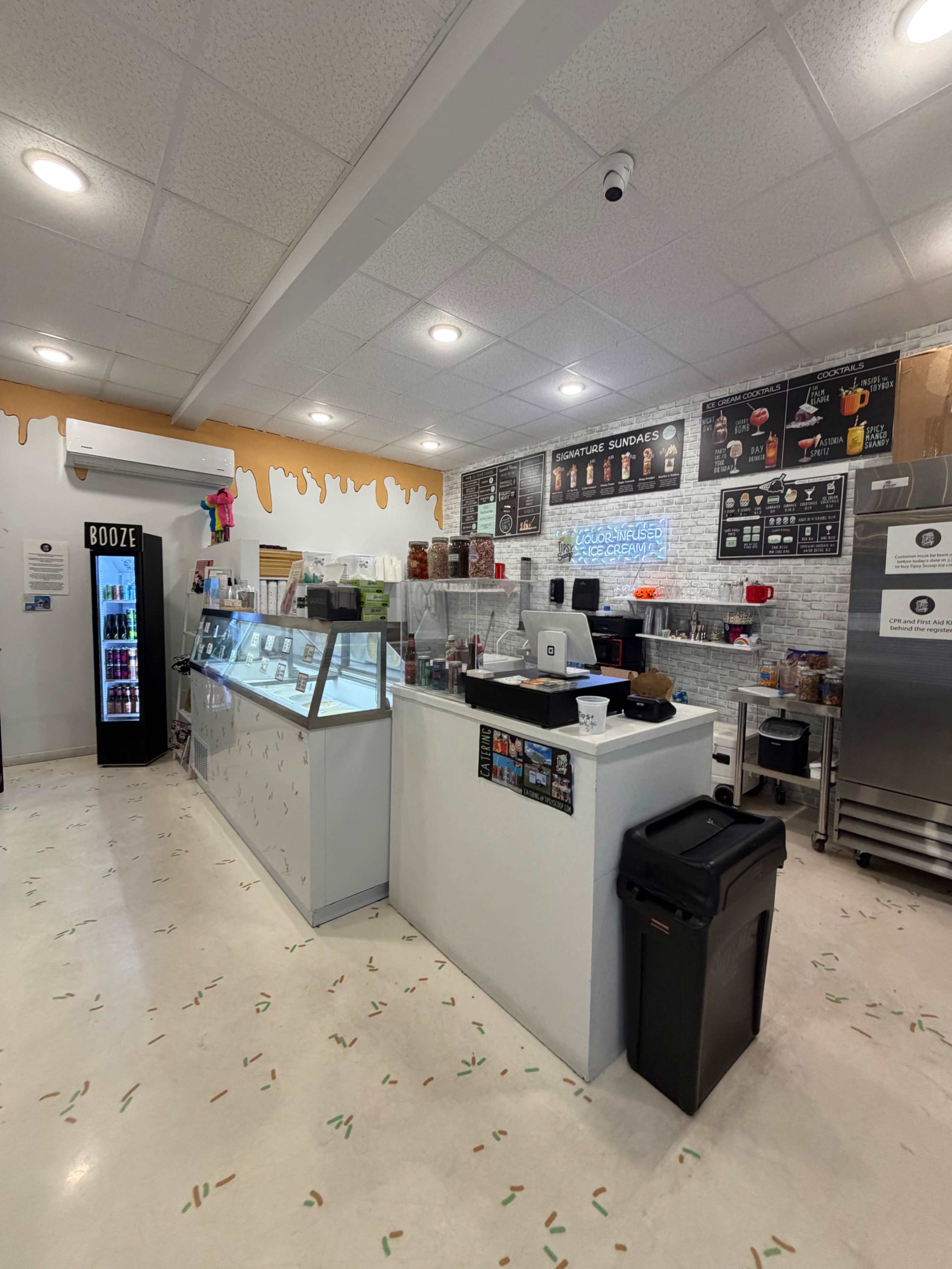 The image shows the interior of a small ice cream shop with a display case, a beverage cooler, and various equipment along the walls.