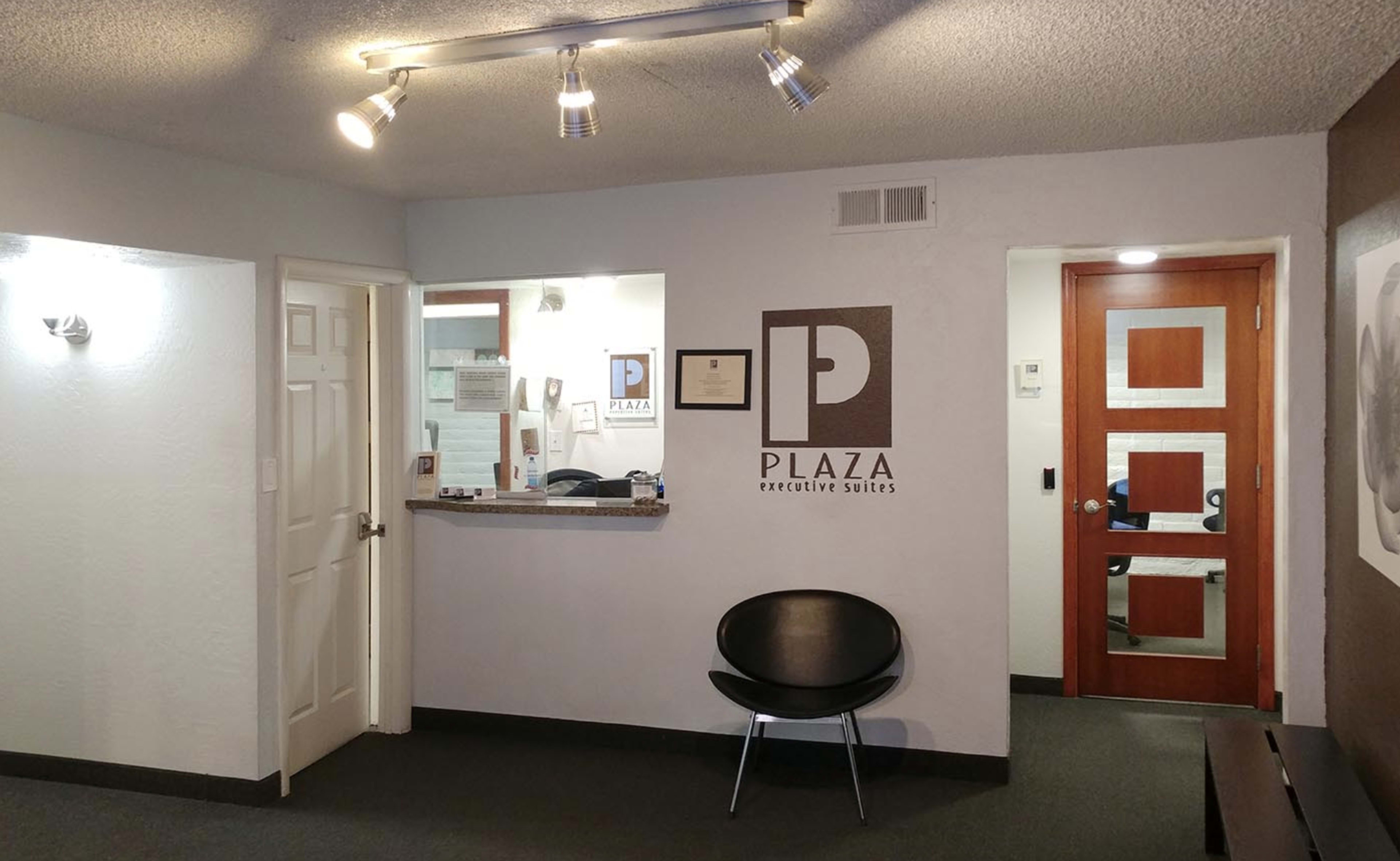 The interior of a reception area featuring a counter, a black chair, and a wall with the logo of "Plaza Executive Suites."