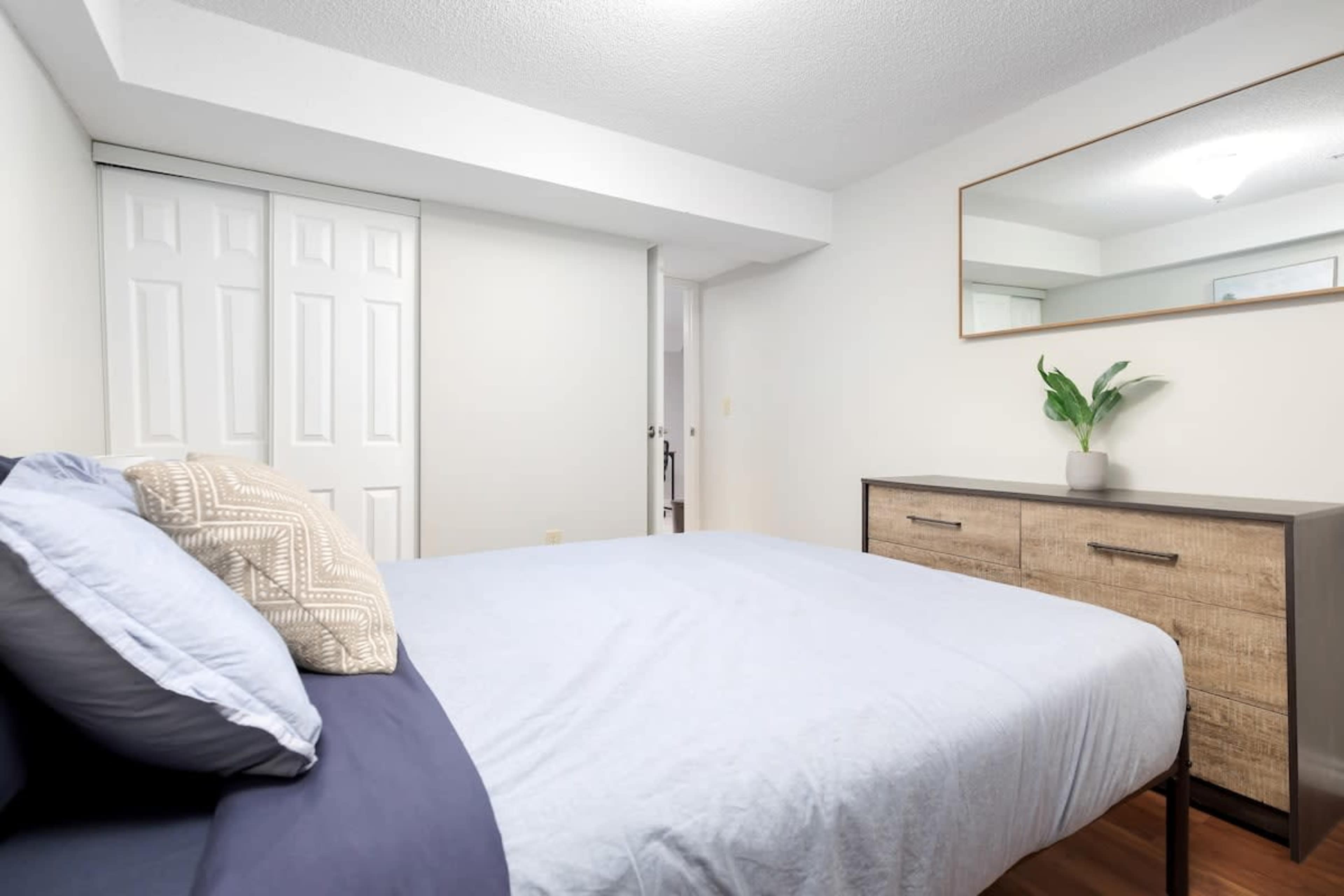 A neatly arranged bedroom featuring a bed with light blue bedding, a wooden dresser, and a mirror on the wall.