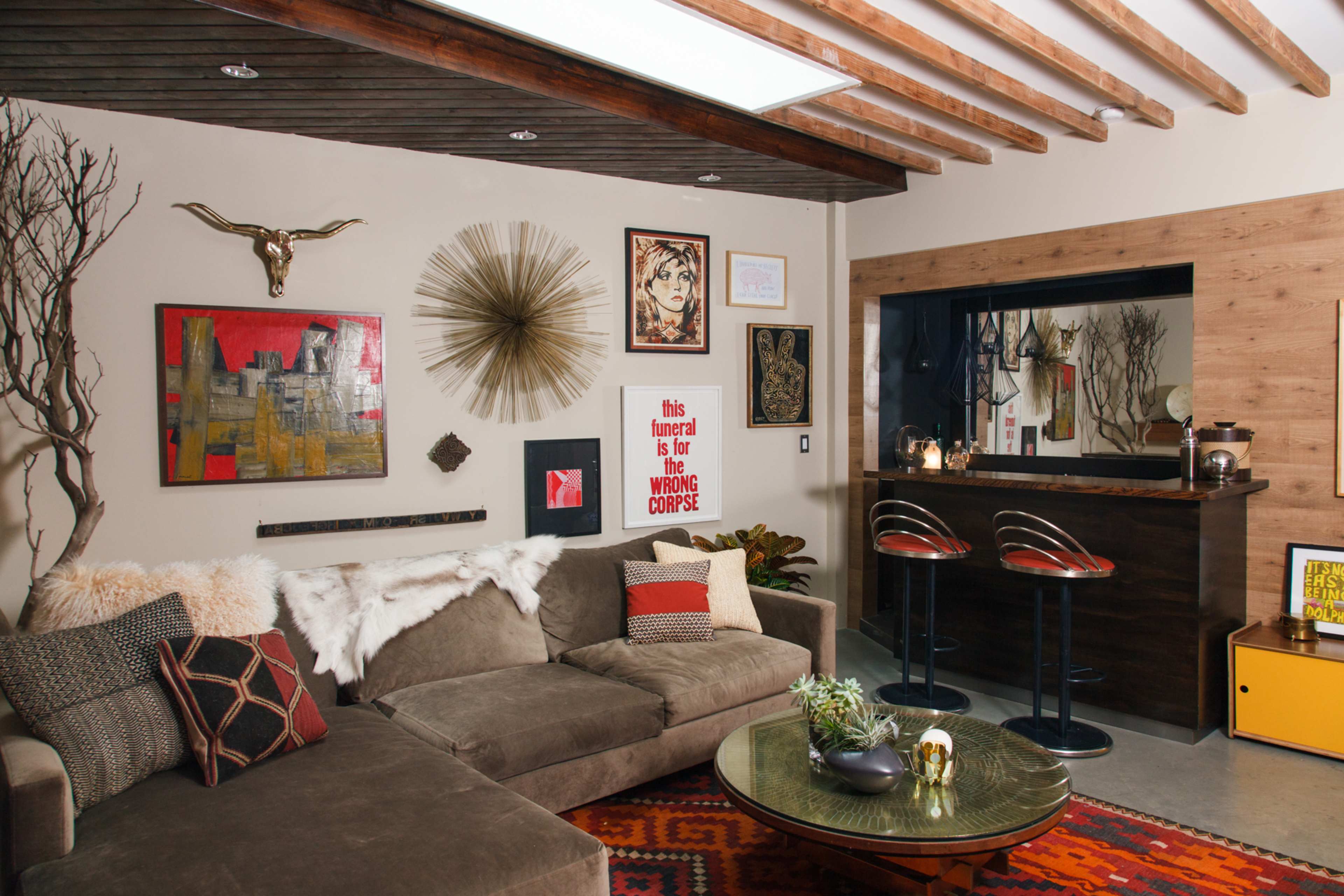 A modern living room with a brown sectional sofa, a decorative rug, a bar area with stools, and various artworks displayed on the walls.