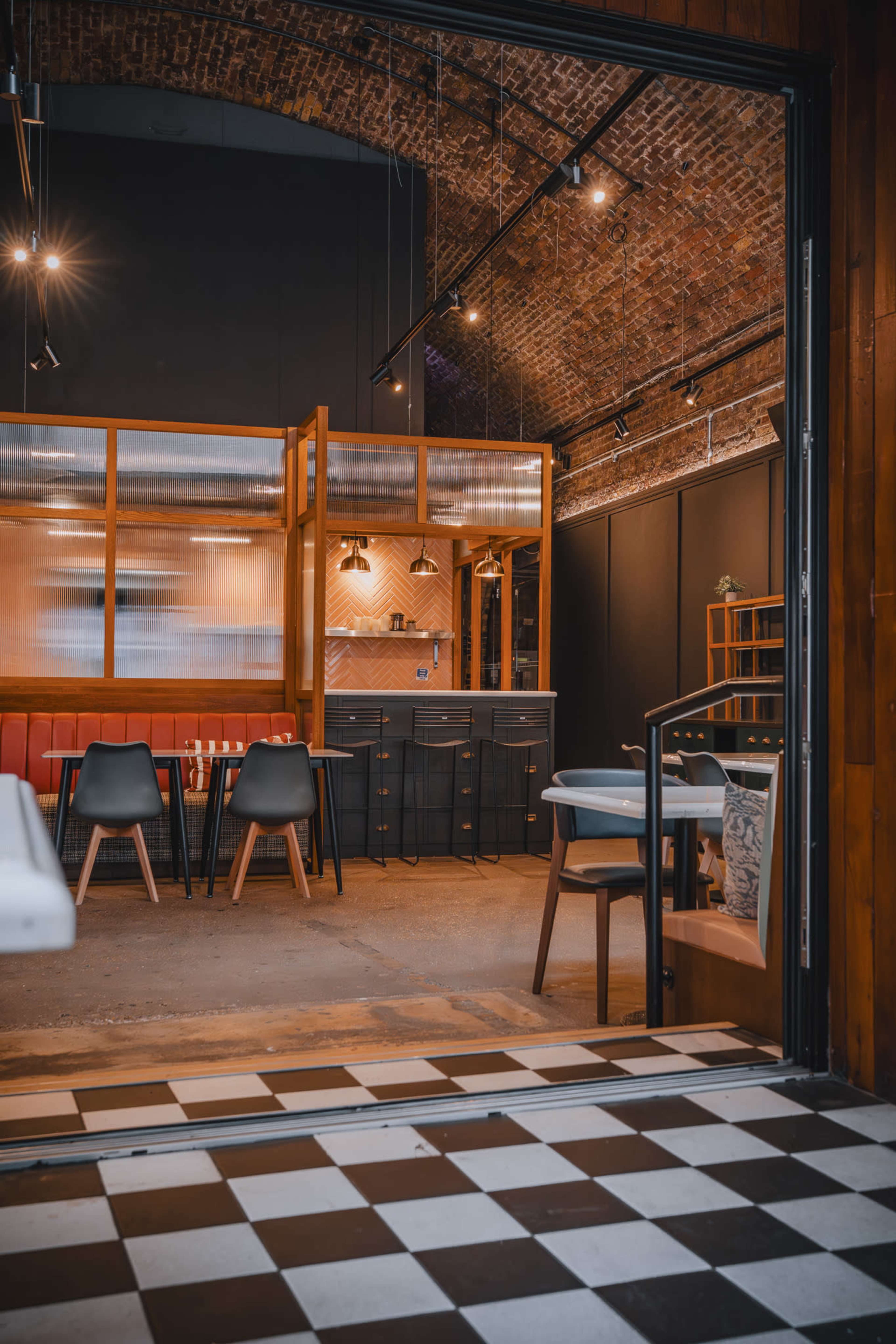 The image shows the interior of a modern restaurant with a brick arch ceiling, a checkered floor, and various dining furniture arranged around an open kitchen area.