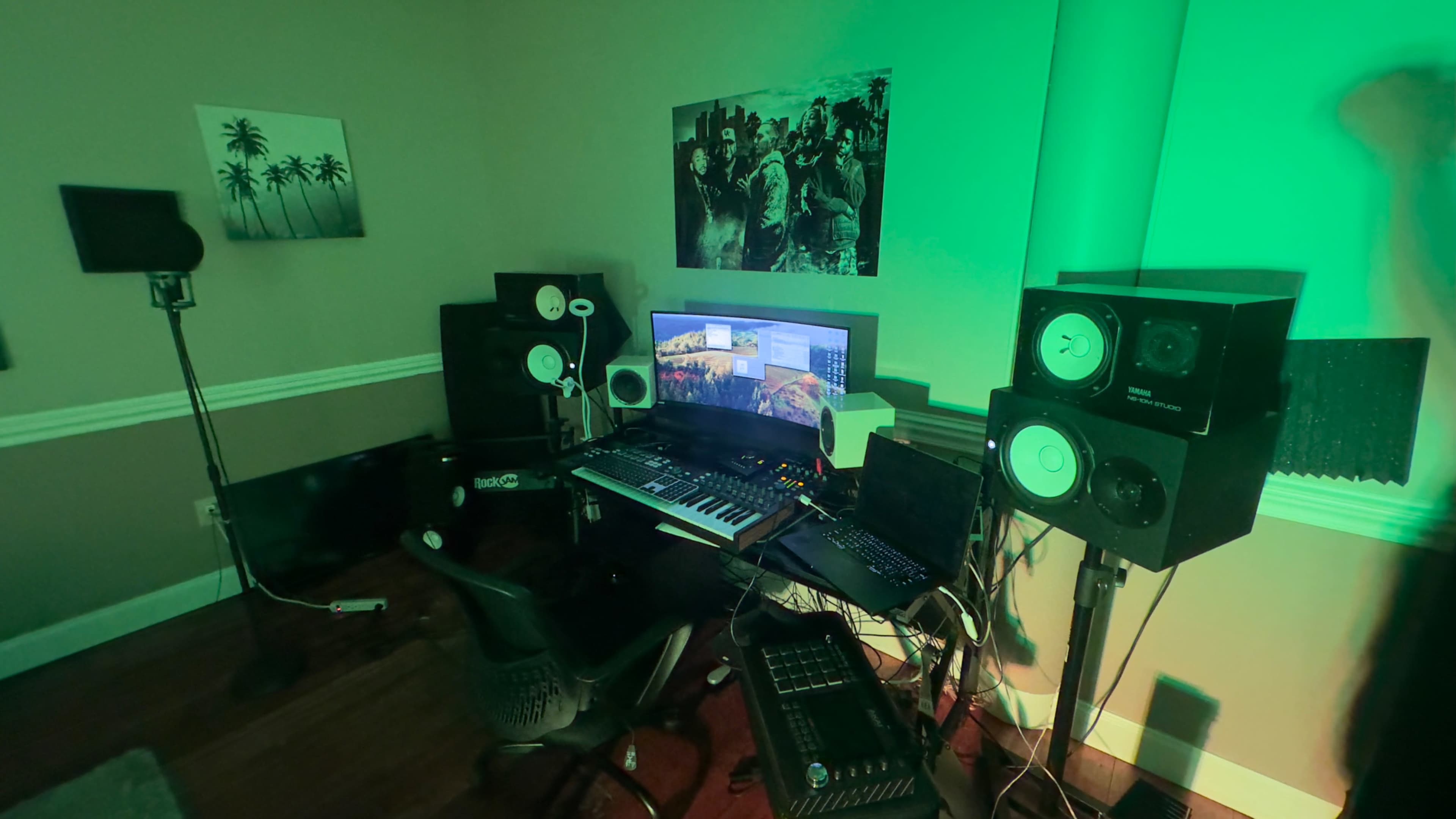 The image shows a music production studio with a computer setup, electronic instruments, and speakers, illuminated by green lighting.