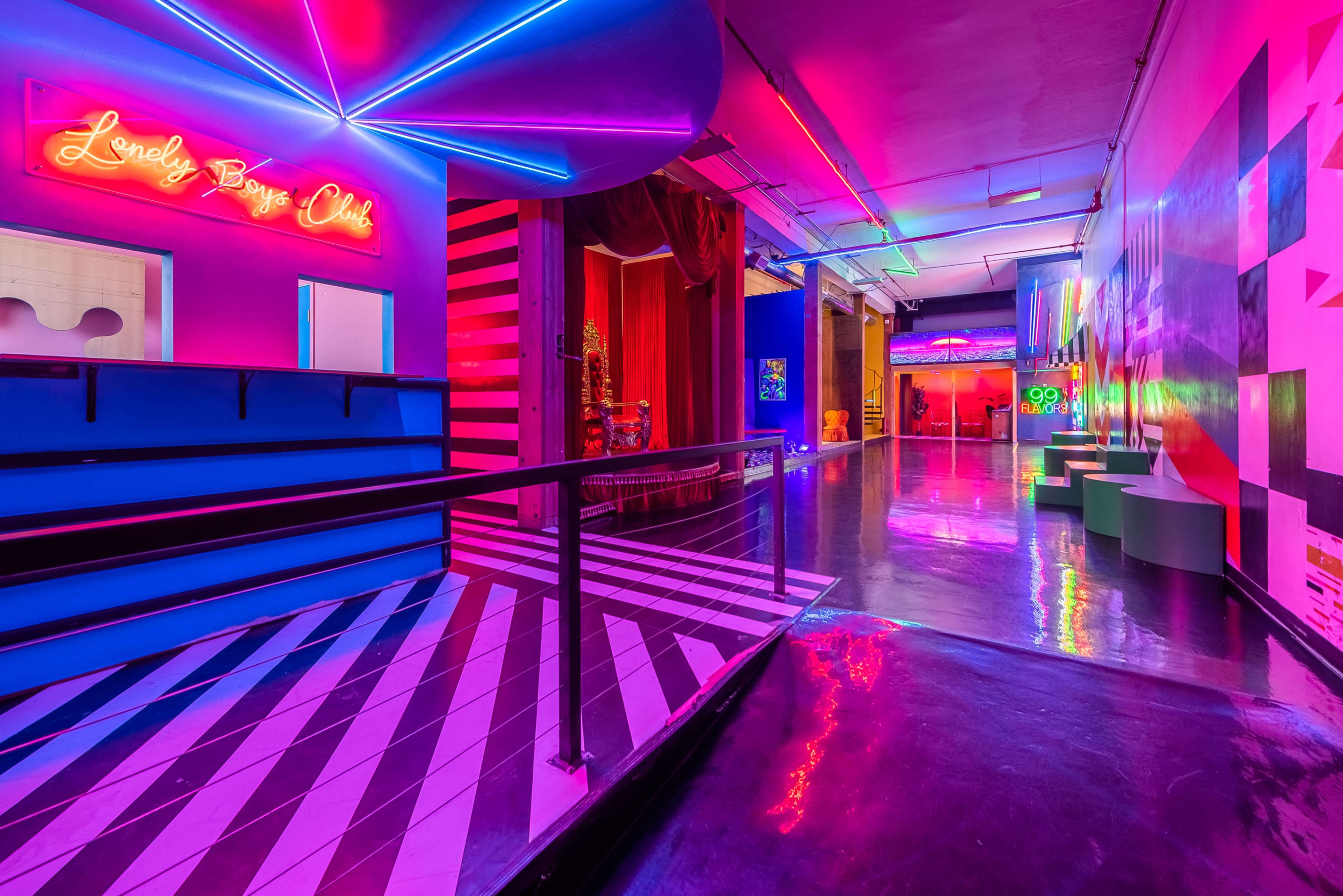 A brightly lit, colorful interior hallway with neon signs, striped walls, and artwork displayed along the sides.