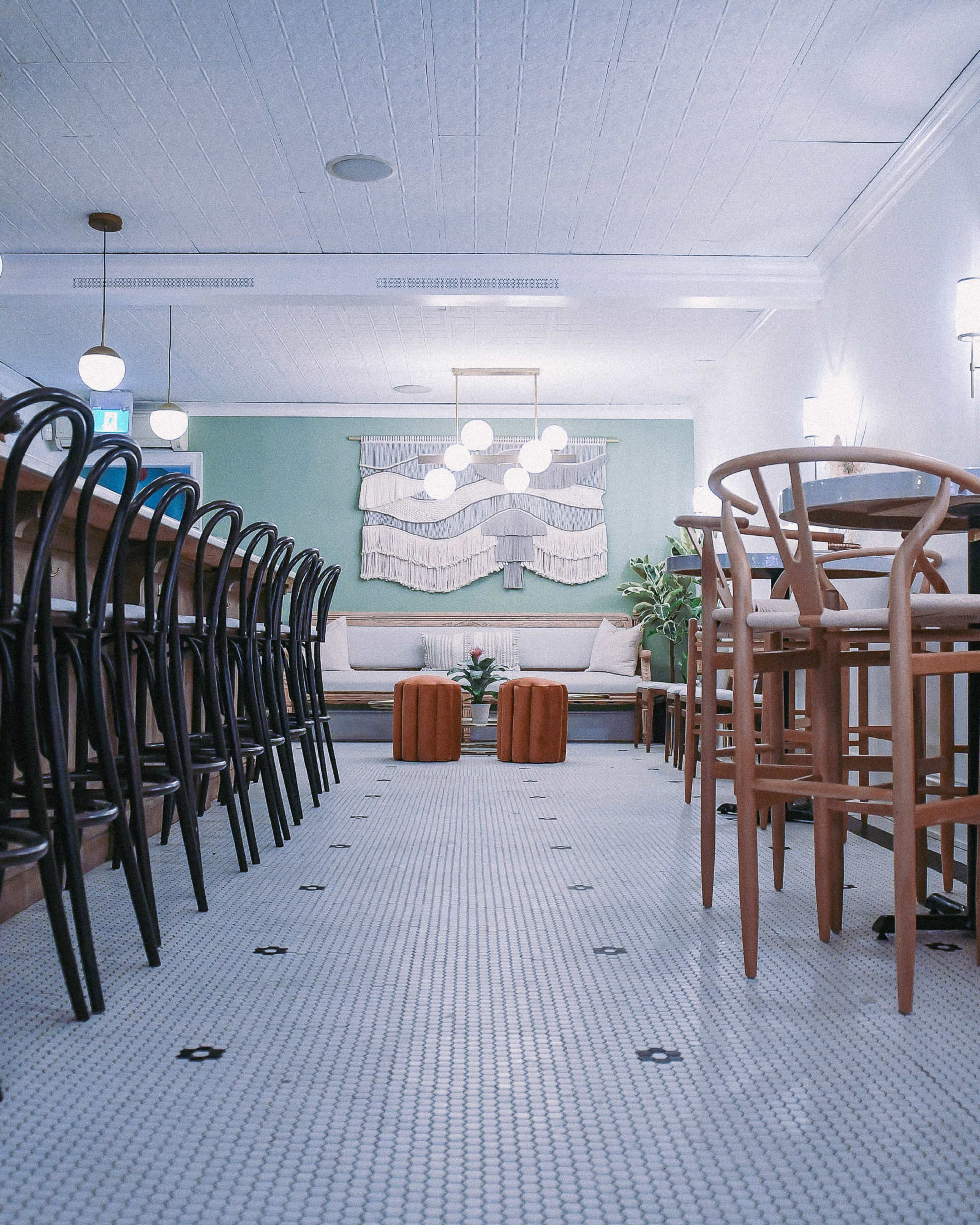 A spacious café interior with rows of chairs and tables, featuring a green wall and a decorative wall hanging.