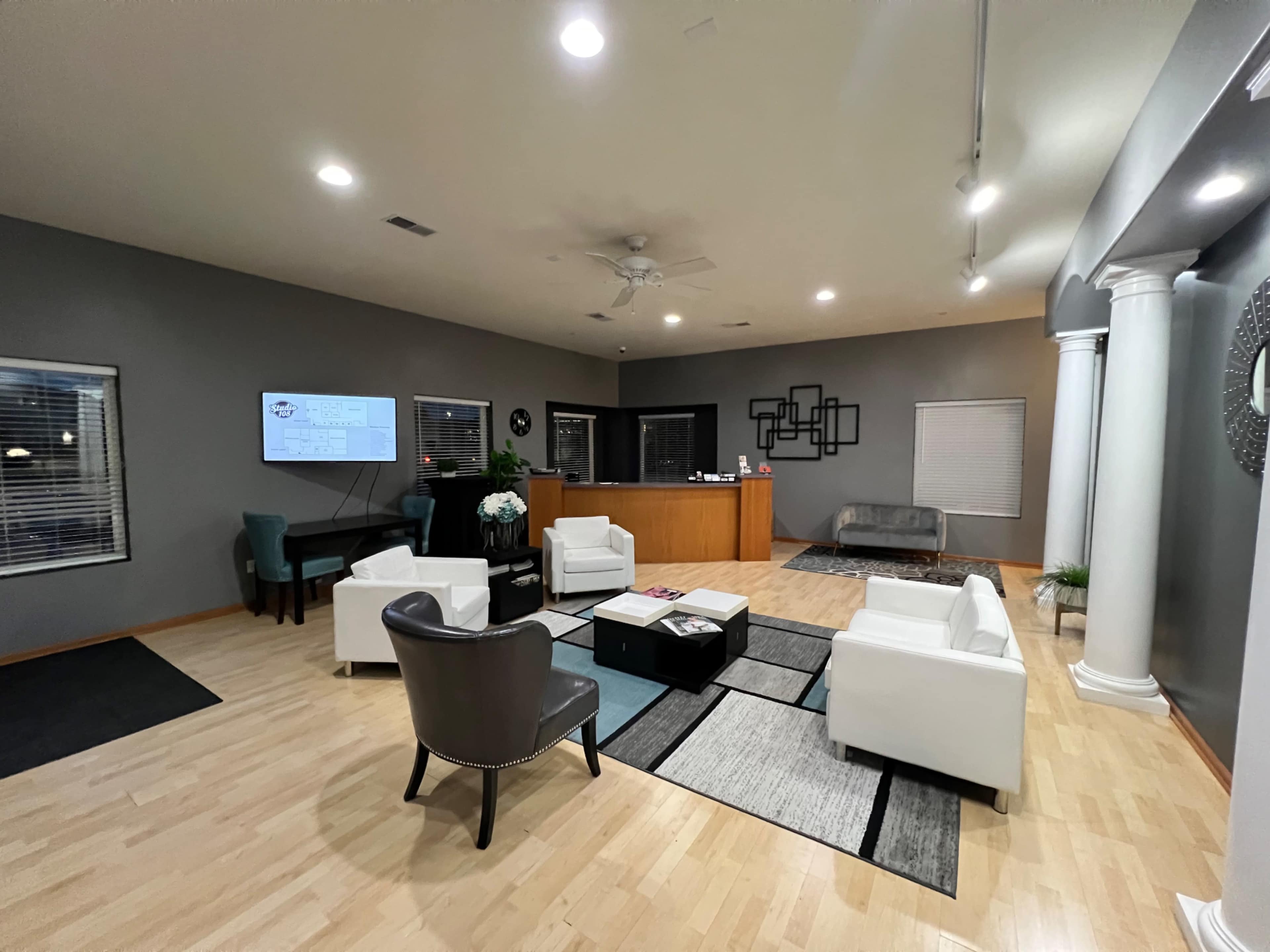 The image shows a modern reception area with white furniture, a dark gray wall, and a wooden front desk.