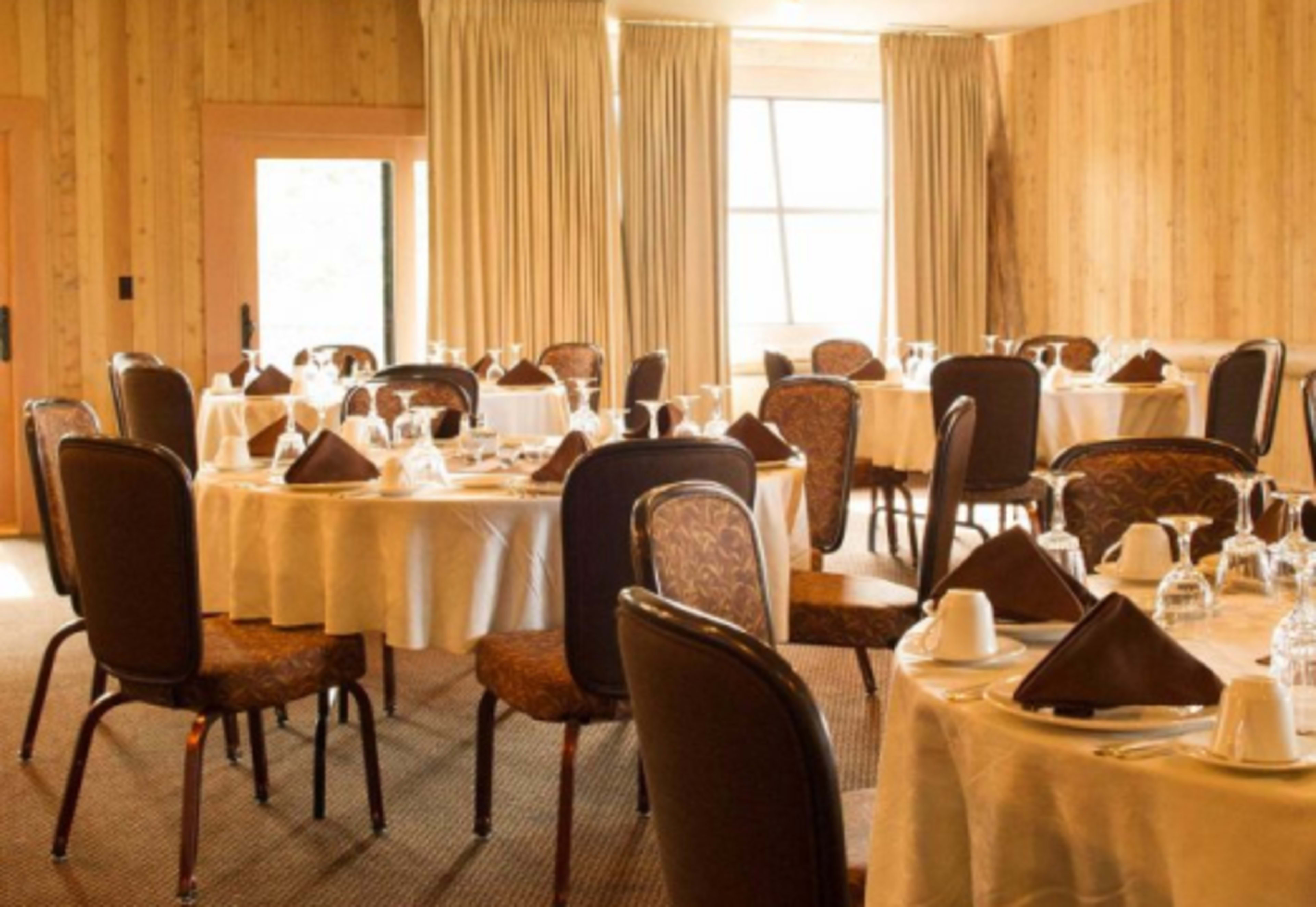 A dining room is arranged with multiple round tables set with white tablecloths, chairs, and glassware.
