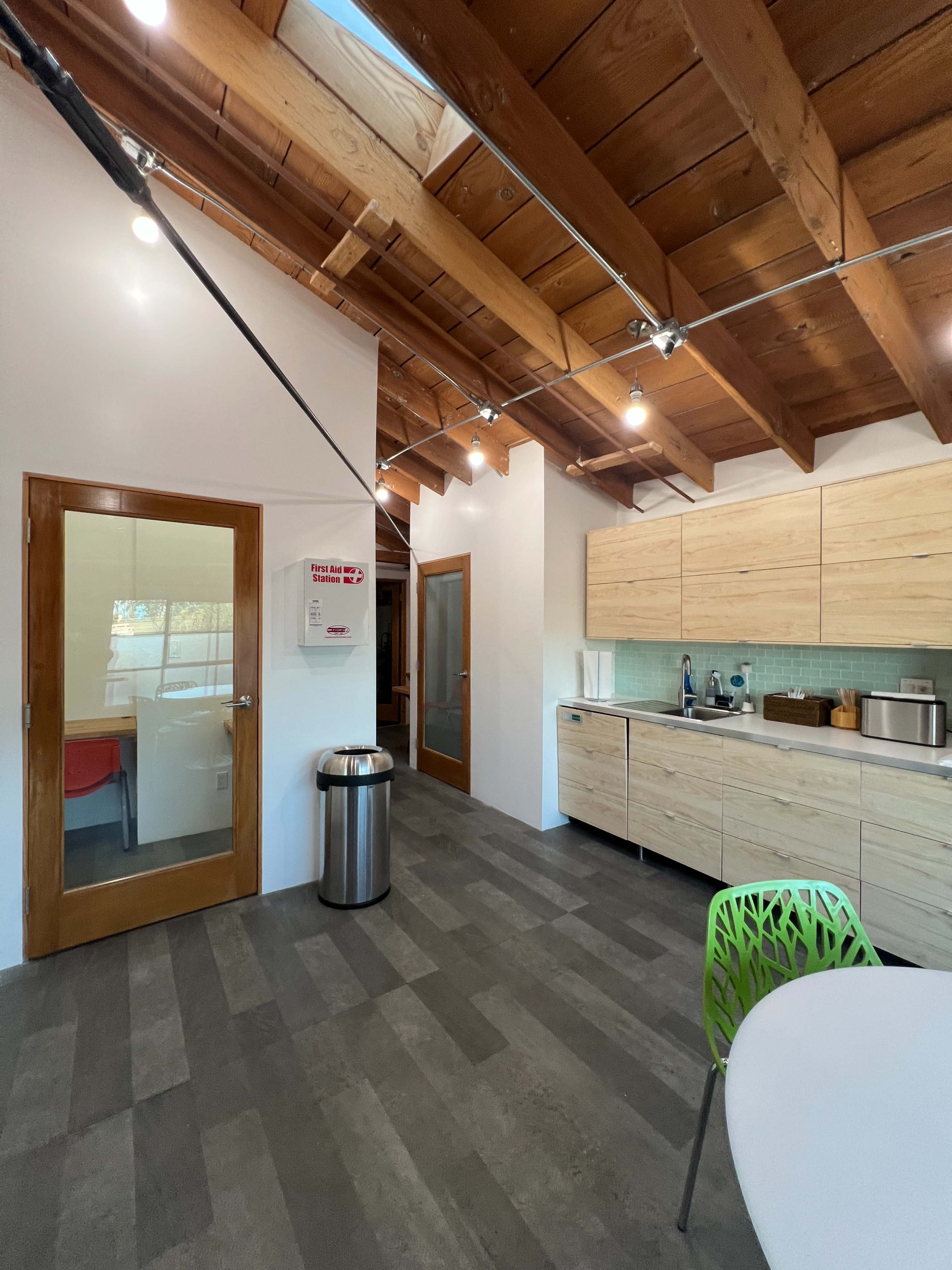 The image shows a modern kitchen with wooden beams, light-colored cabinetry, and a round dining table.