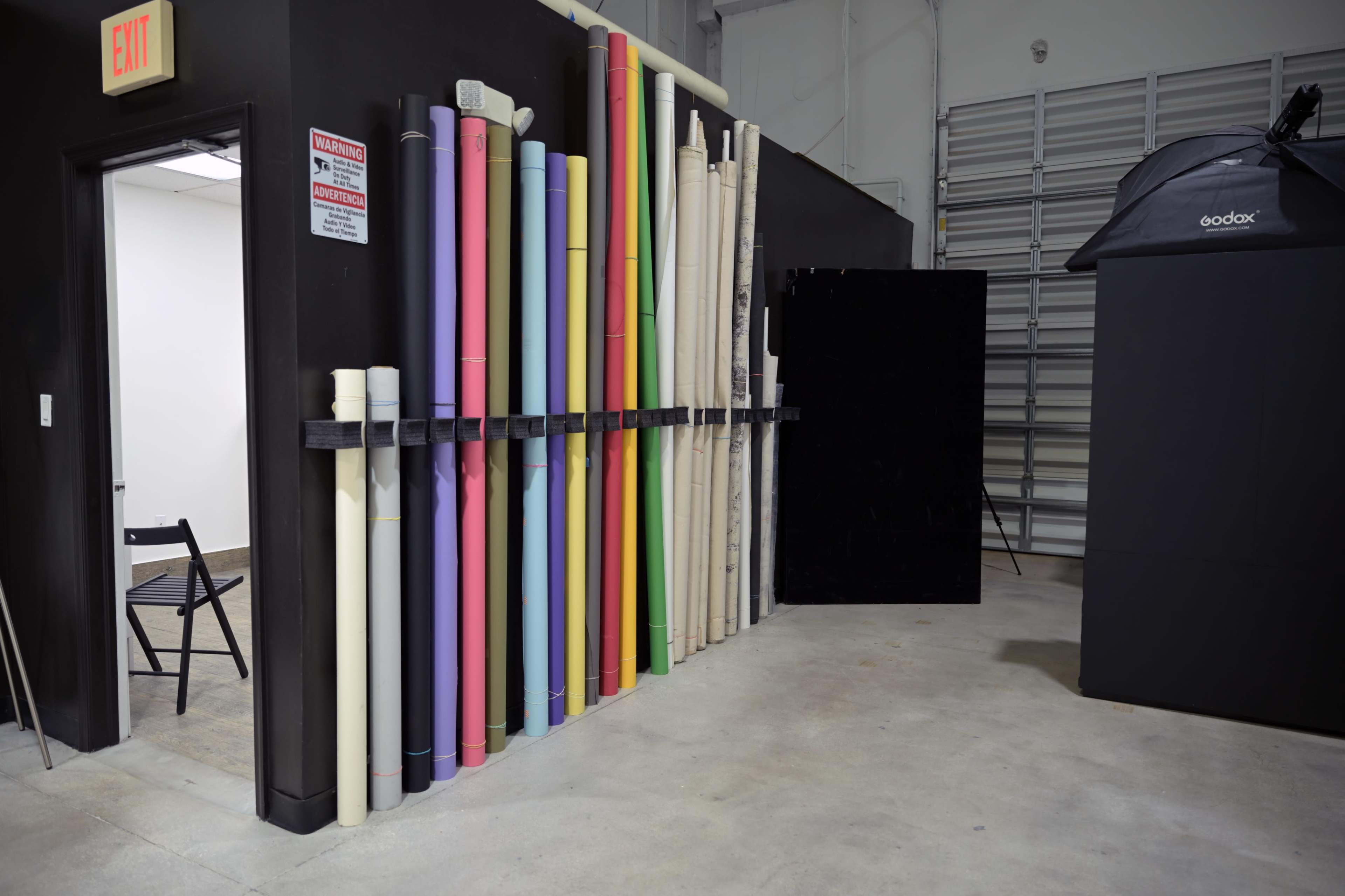 The image shows a photography studio interior with a collection of rolled backdrop paper in various colors organized against a black wall.