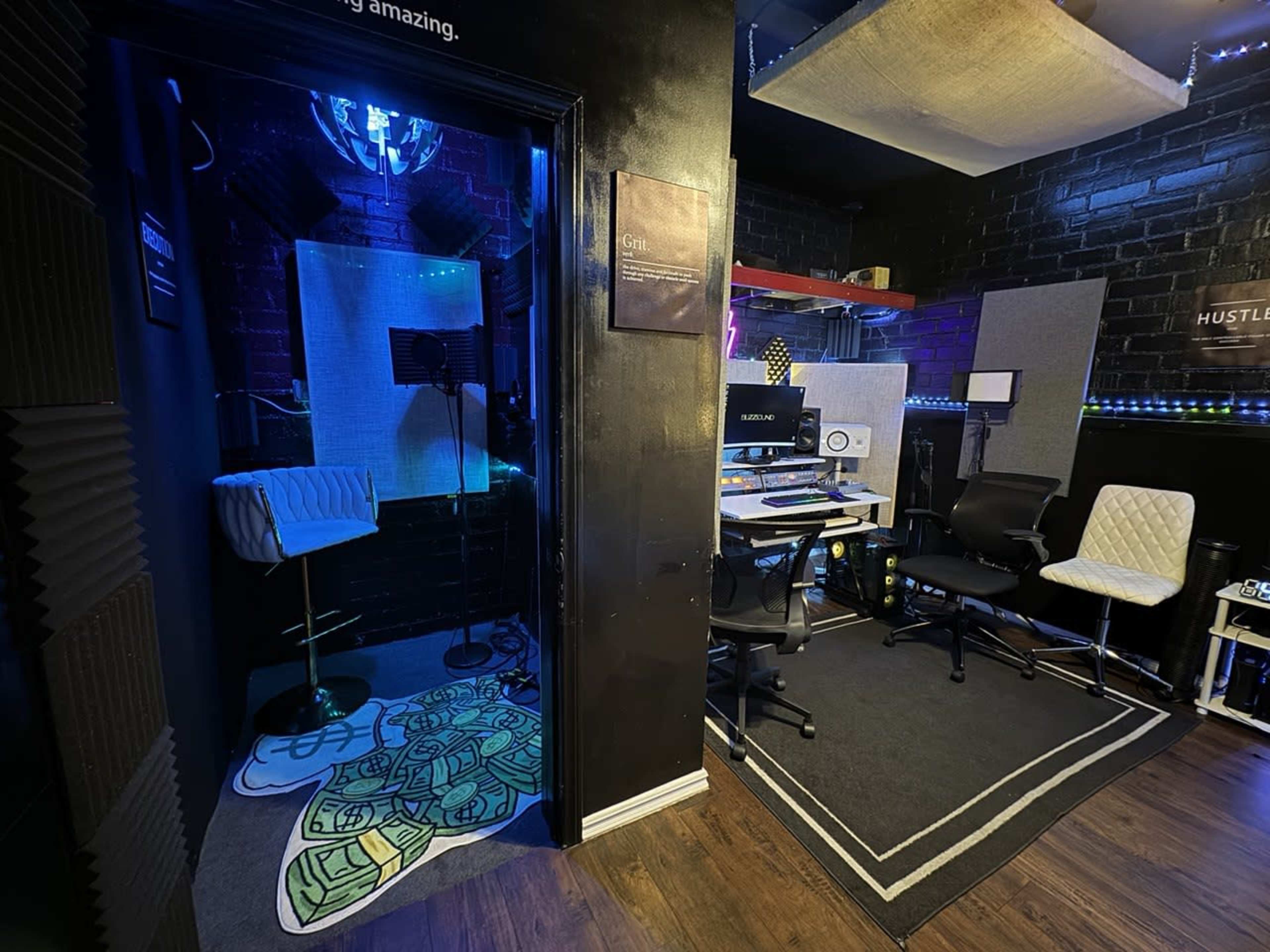 The image shows a music studio divided into two areas: a recording booth with blue lighting and a workspace equipped with a computer and chairs.