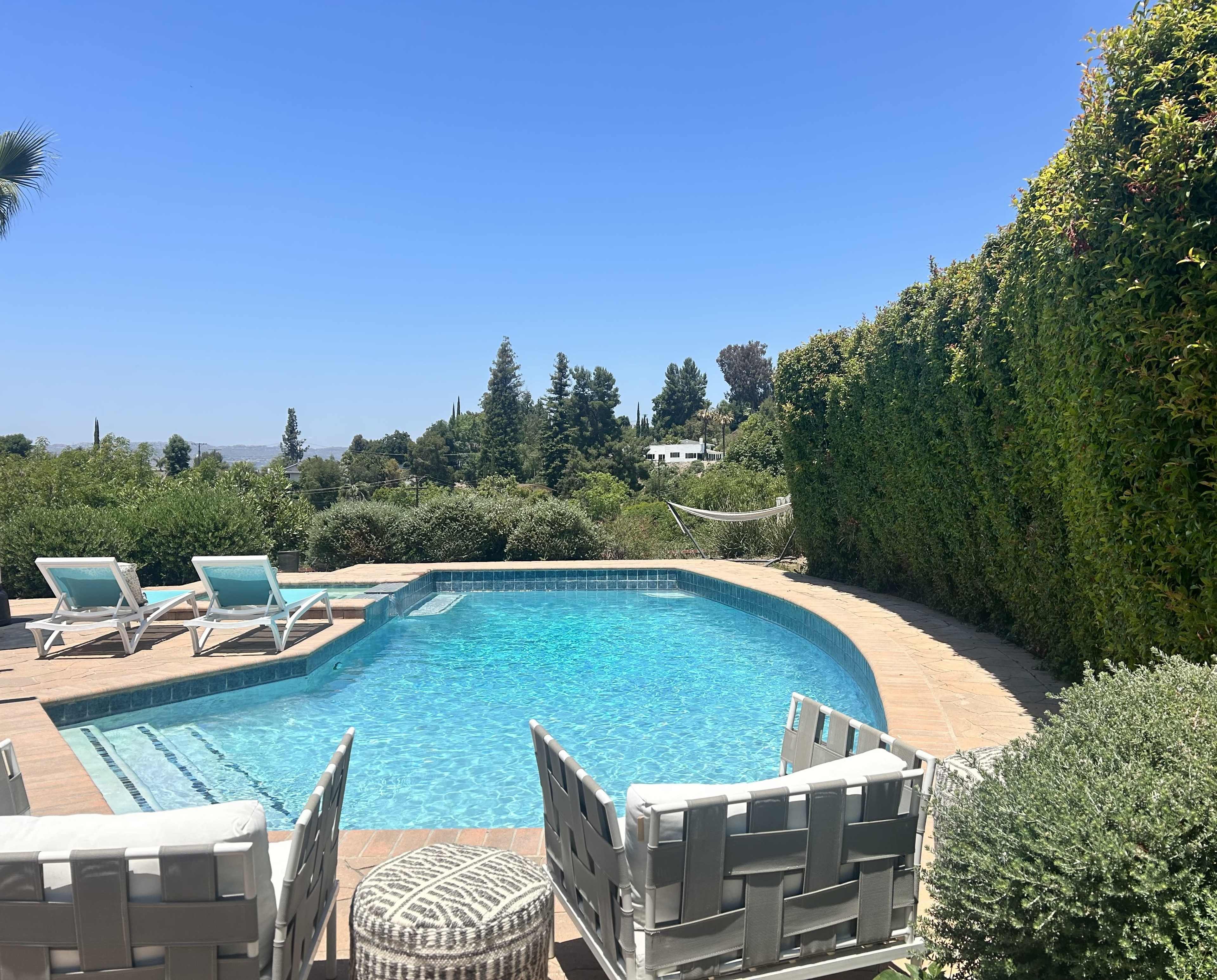 A swimming pool surrounded by lounge chairs and greenery under a clear blue sky.