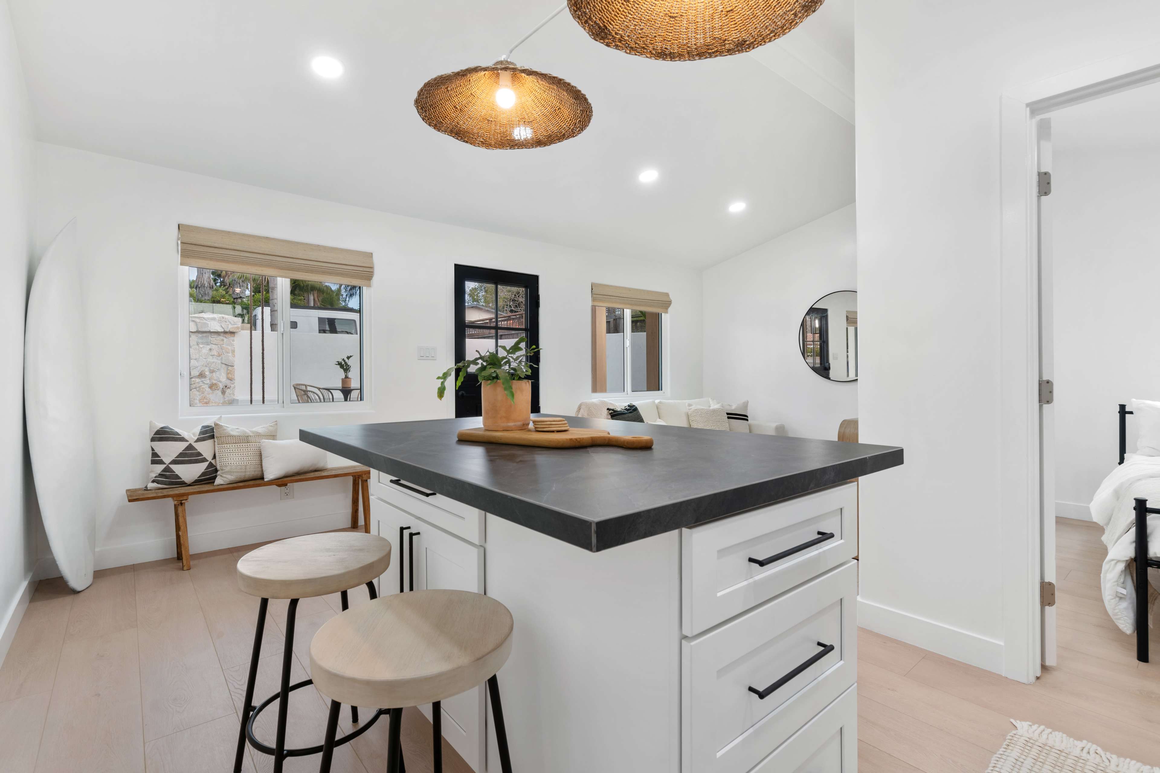 A modern kitchen features a central island with a dark countertop, two wooden stools, and pendant lighting above.