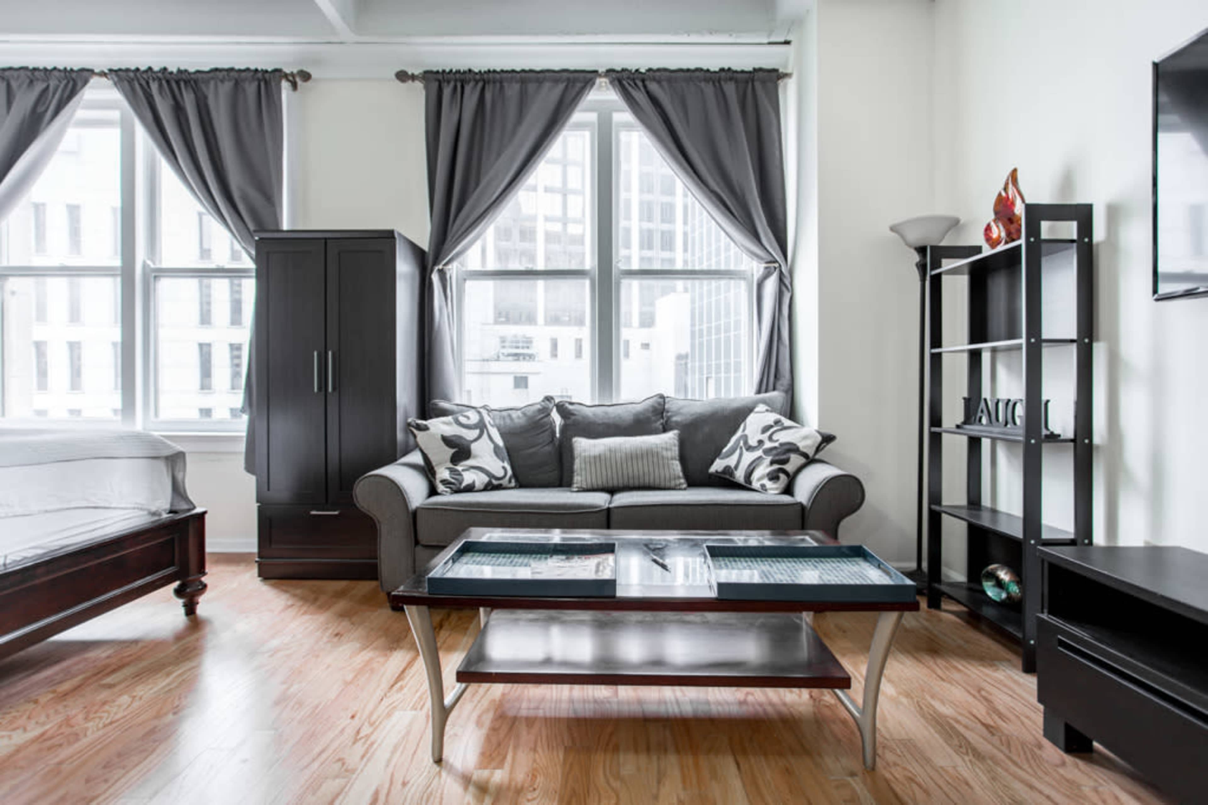 A modern living space featuring a gray sofa, a glass coffee table, and large windows with curtains.