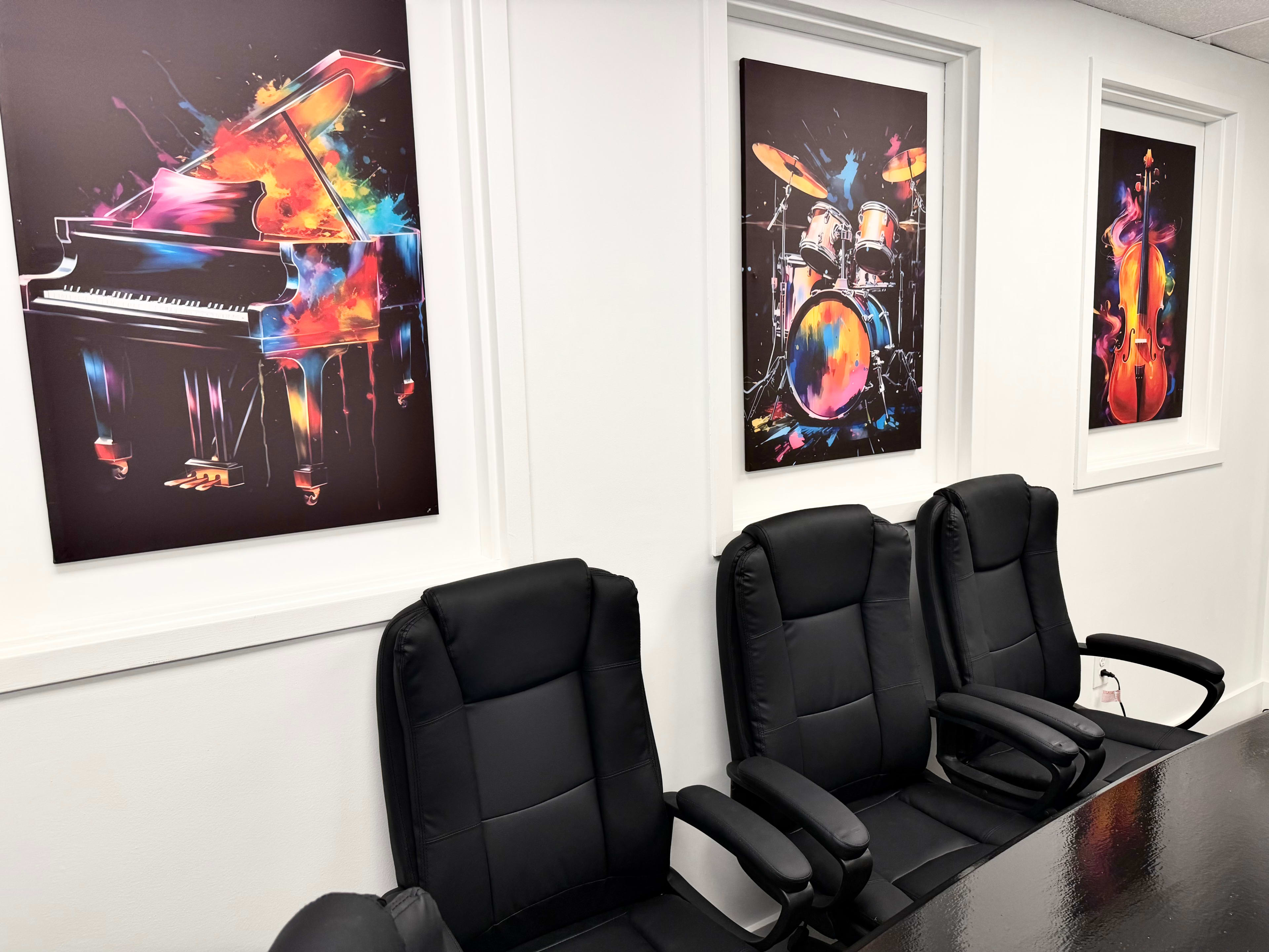 The image shows a conference room featuring three colorful musical instrument artworks on the walls and three black office chairs arranged around a table.