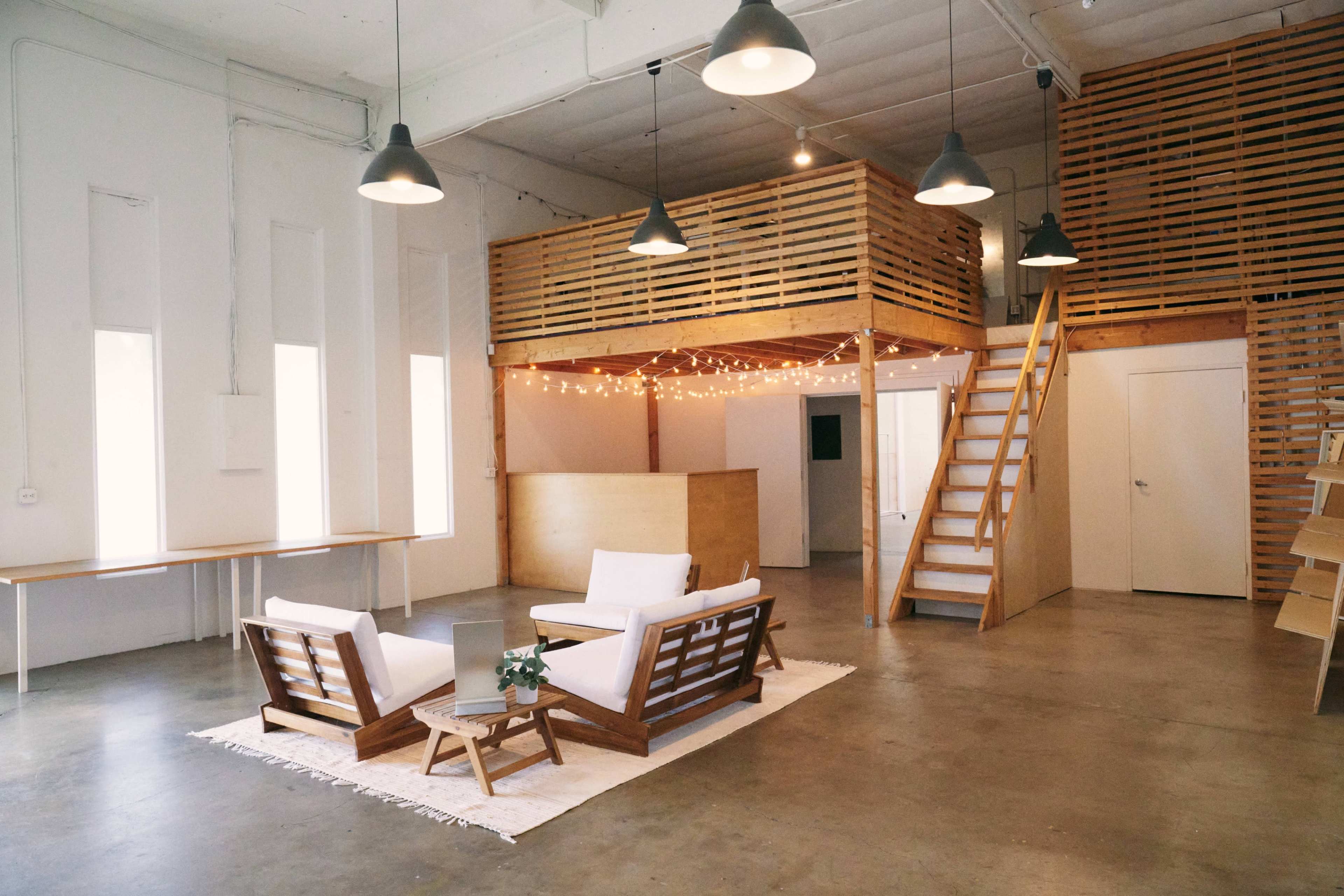 A spacious, modern interior with a seating area featuring two white chairs, a wooden counter, and a lofted space accessed by stairs.