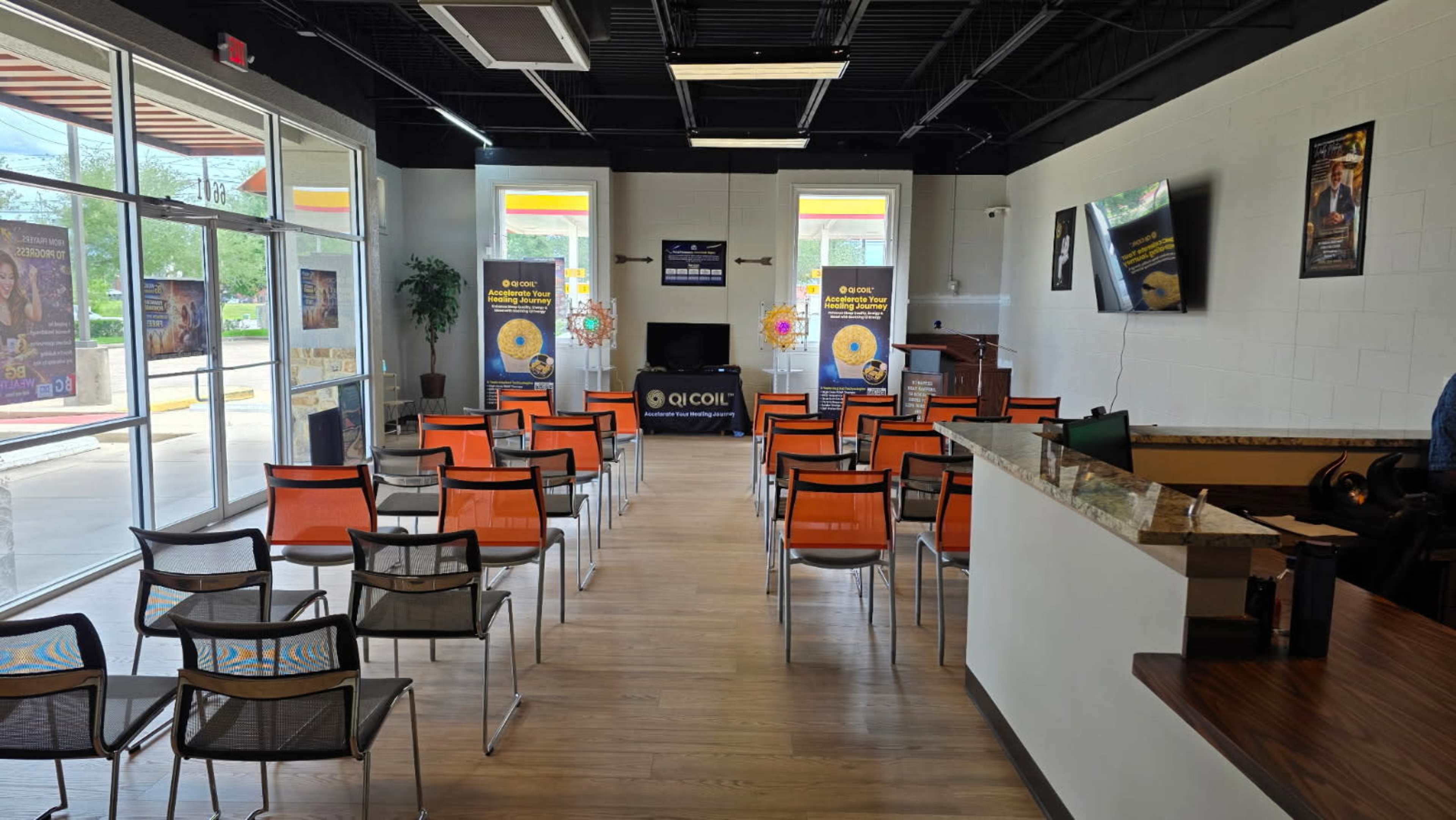 The image shows a spacious waiting area with orange chairs arranged in rows, a reception desk, and promotional banners on the walls.