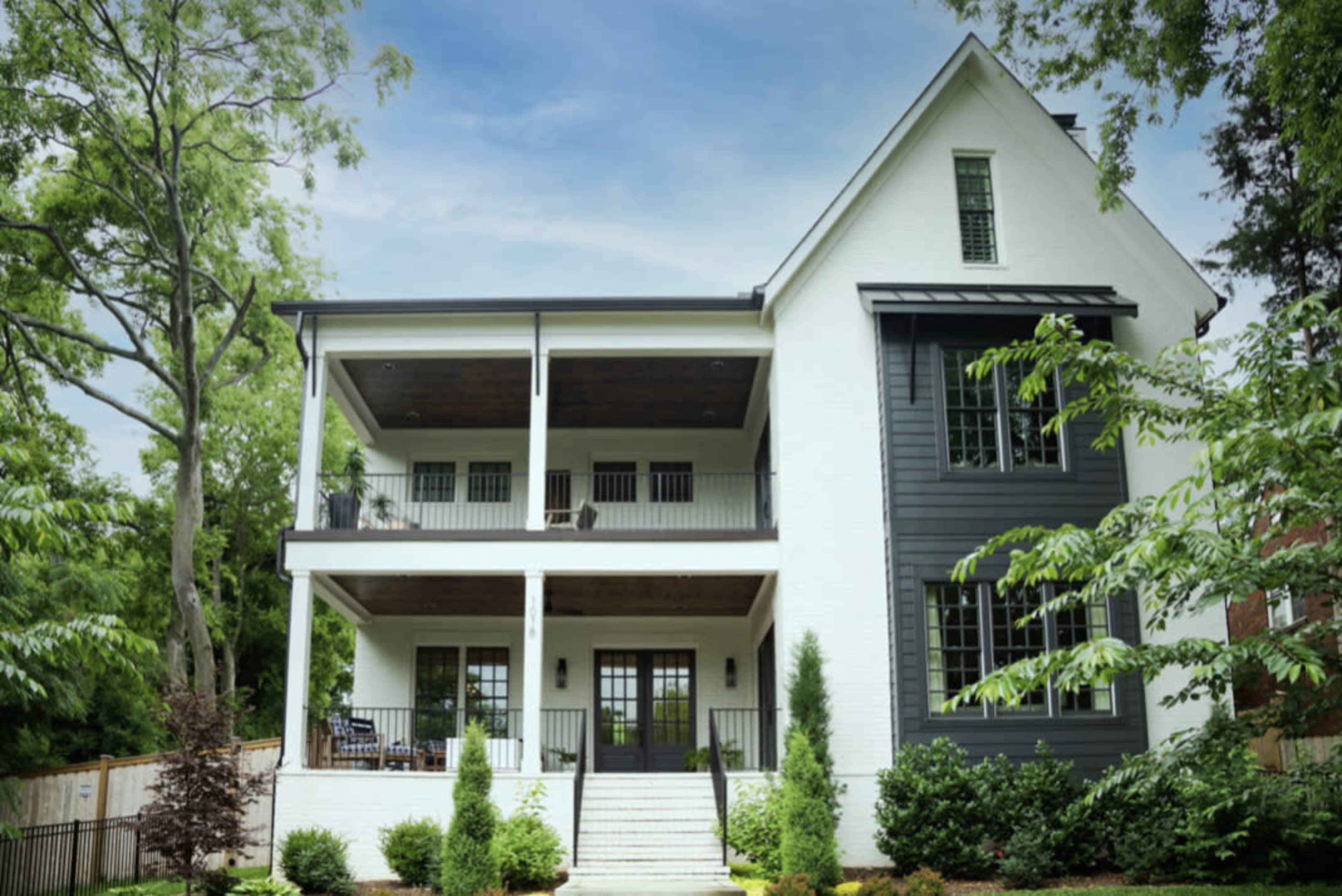 A modern three-story house features a white exterior with dark accents and a spacious porch.