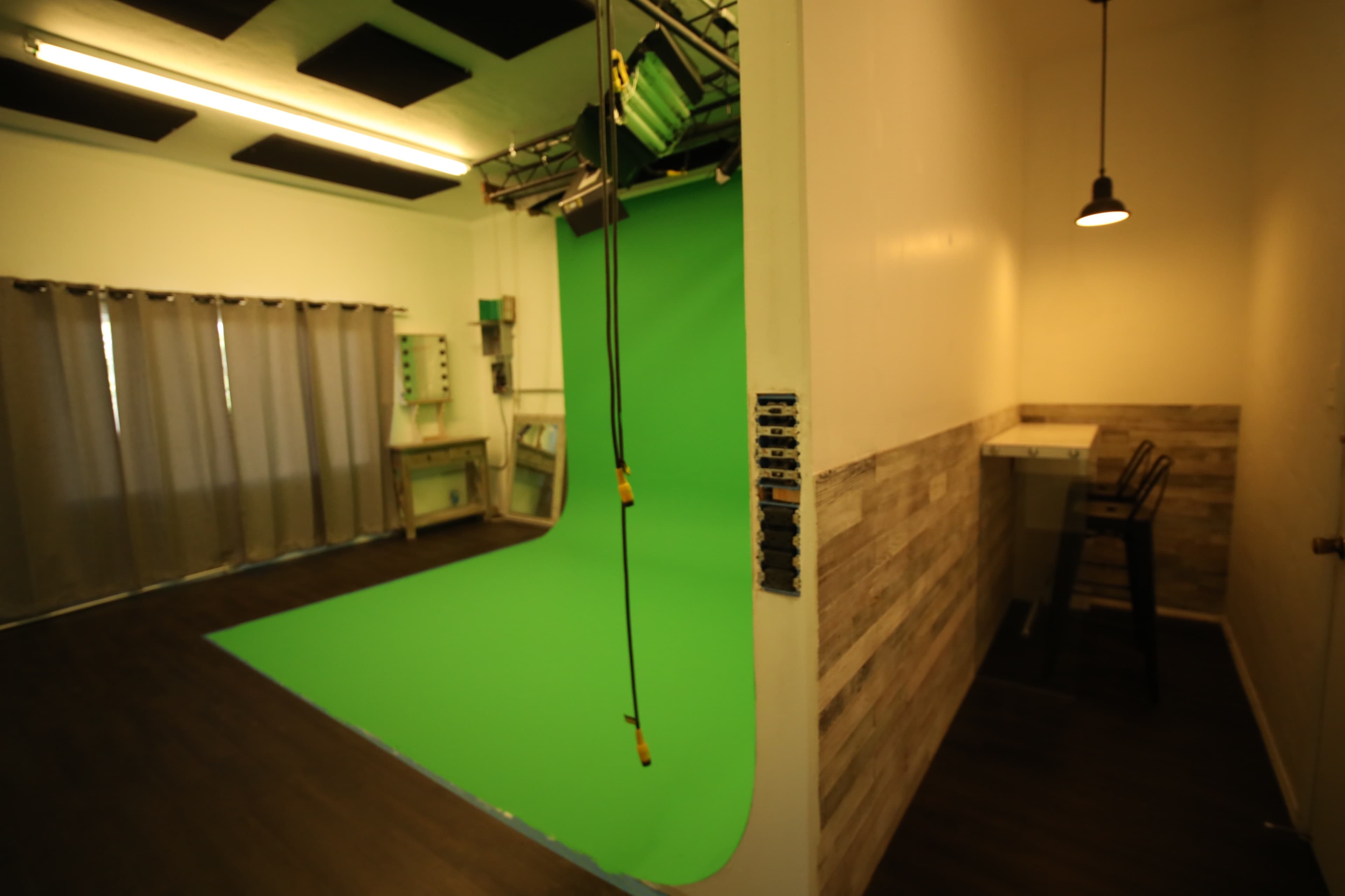 A studio with a green backdrop and a small workspace featuring a table and a chair.