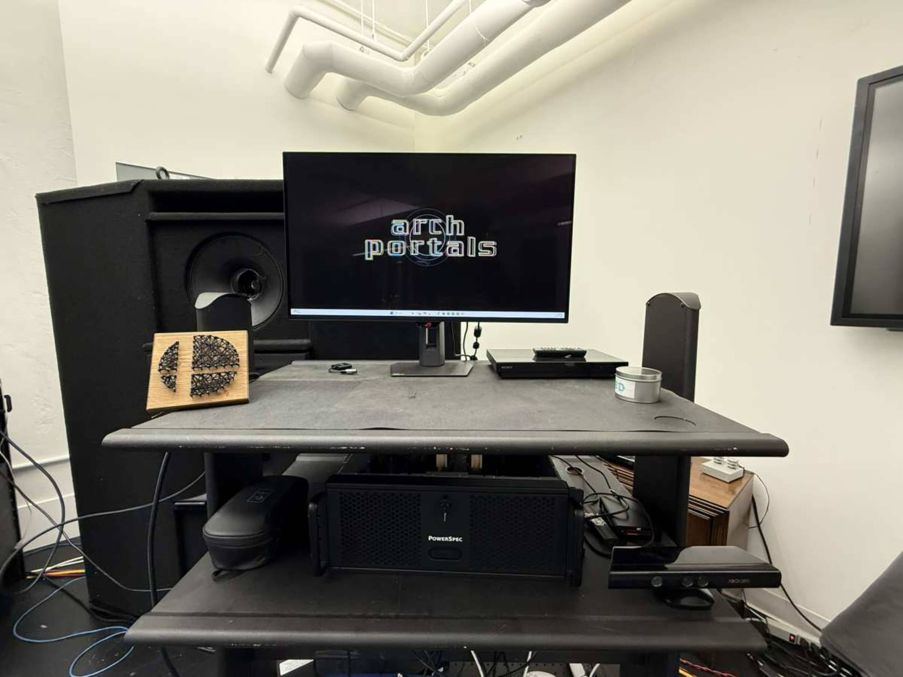 A computer monitor displaying the text "arch portals" is positioned on a desk with various electronic devices and audio equipment in a room.