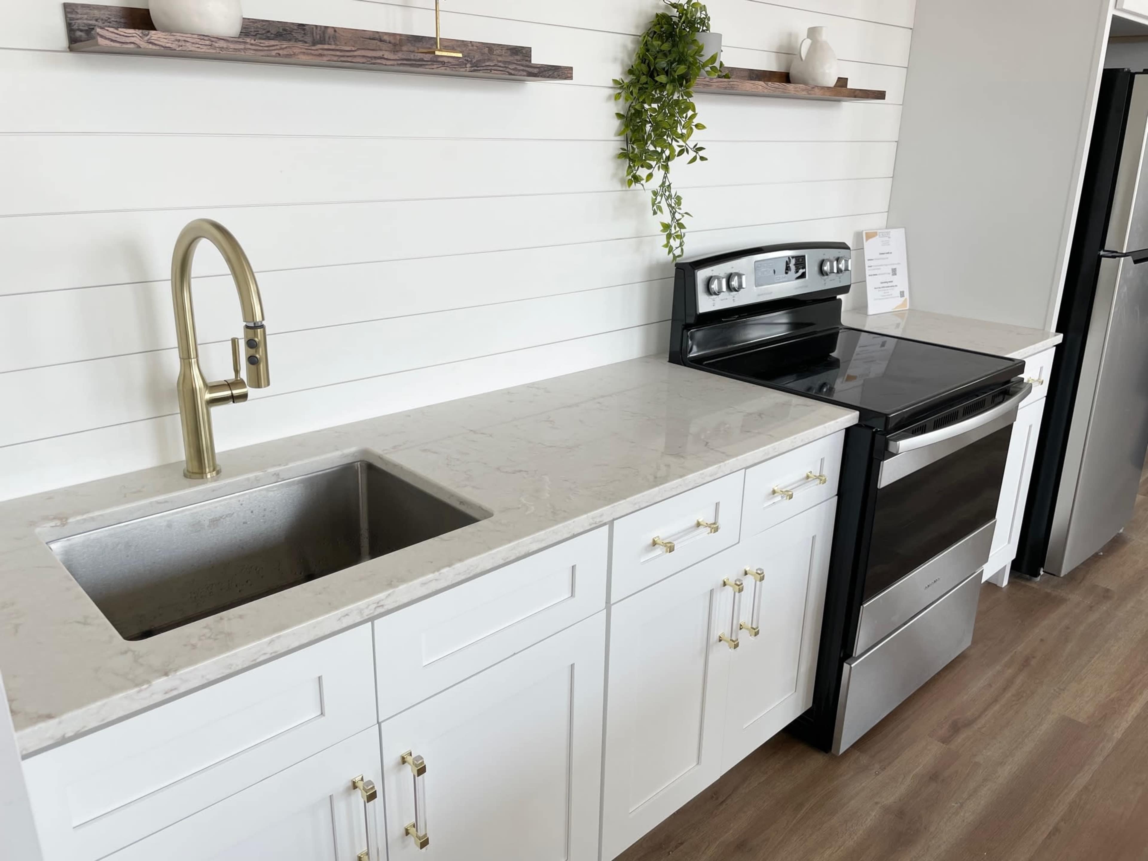 The image shows a modern kitchen with a stainless steel sink, a black stove, and white cabinetry against a shiplap wall.
