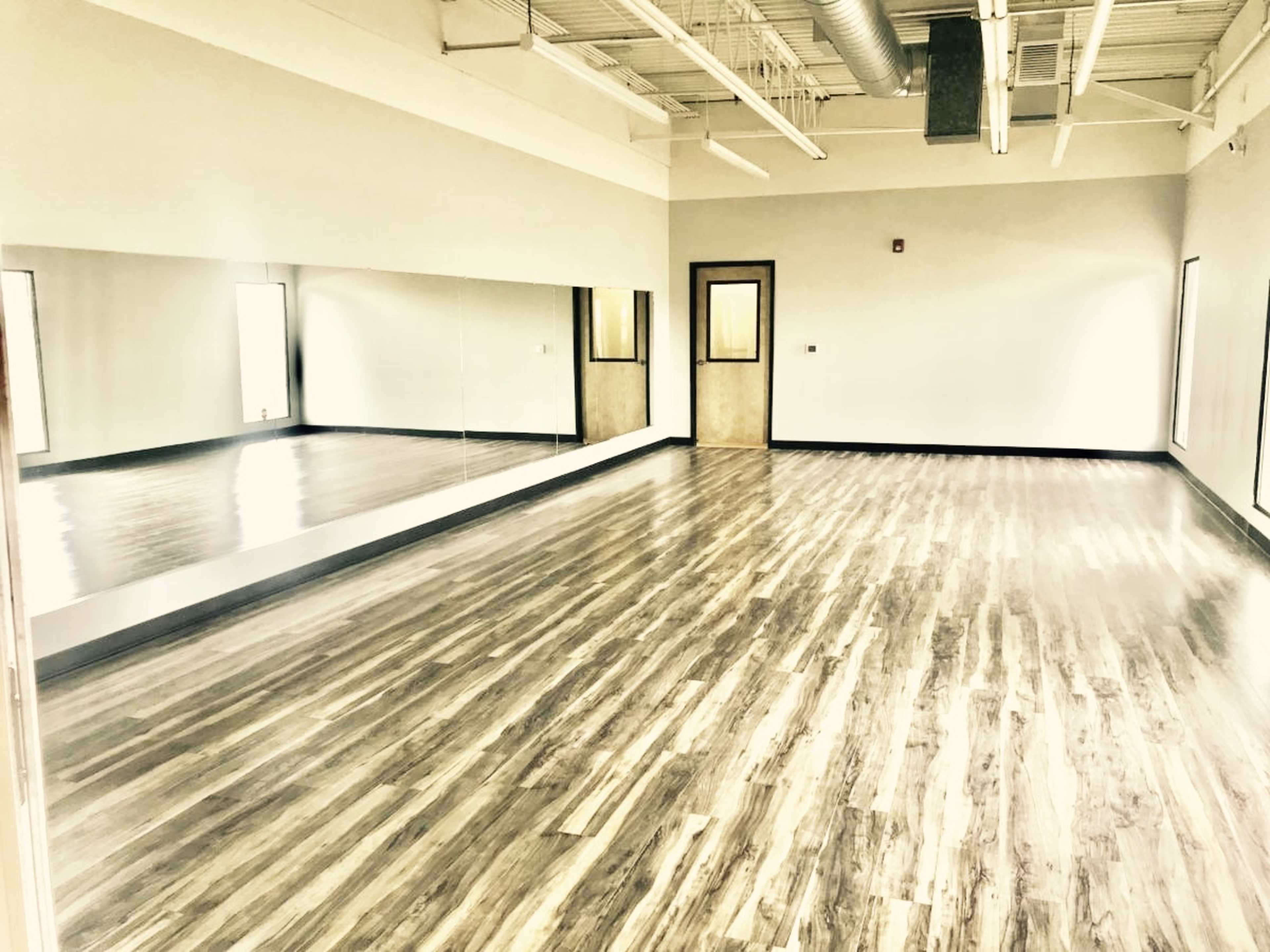 An empty room with hardwood floors and a large mirror on one wall.
