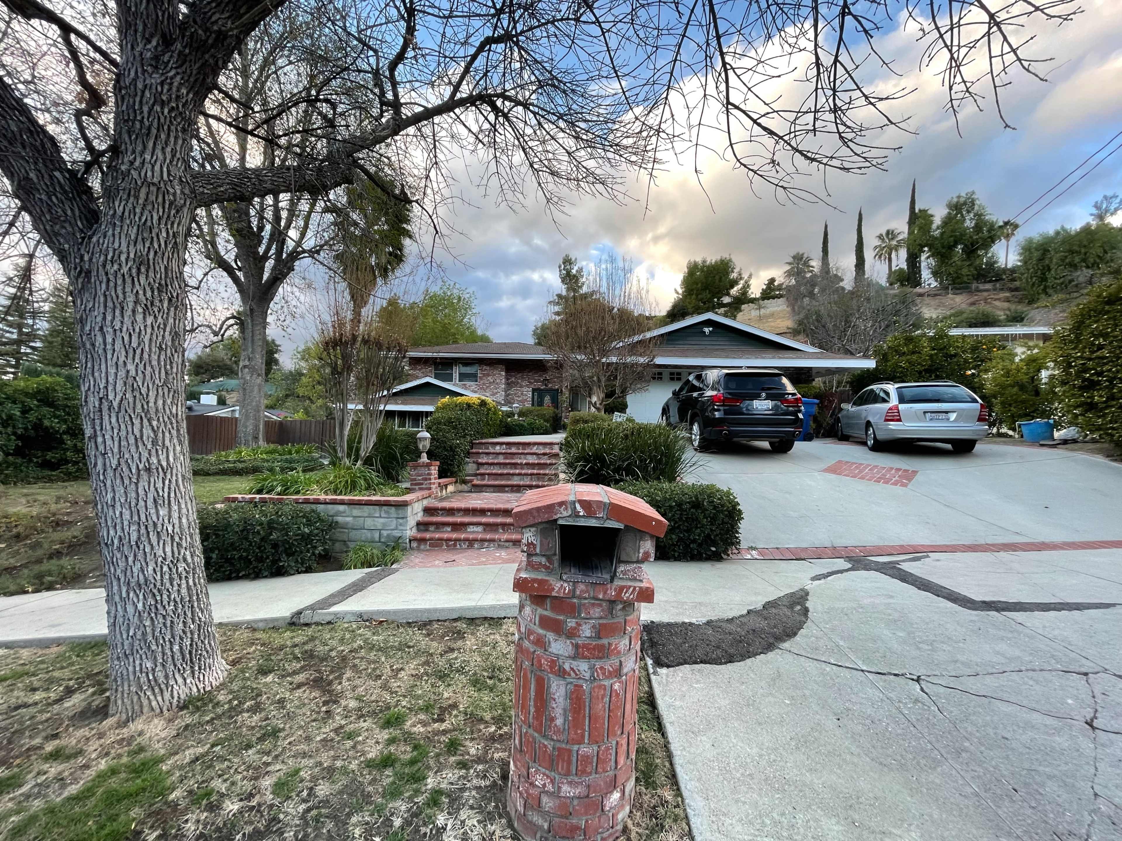 The image shows a residential home with a driveway accommodating two cars and a brick mailbox in the foreground.