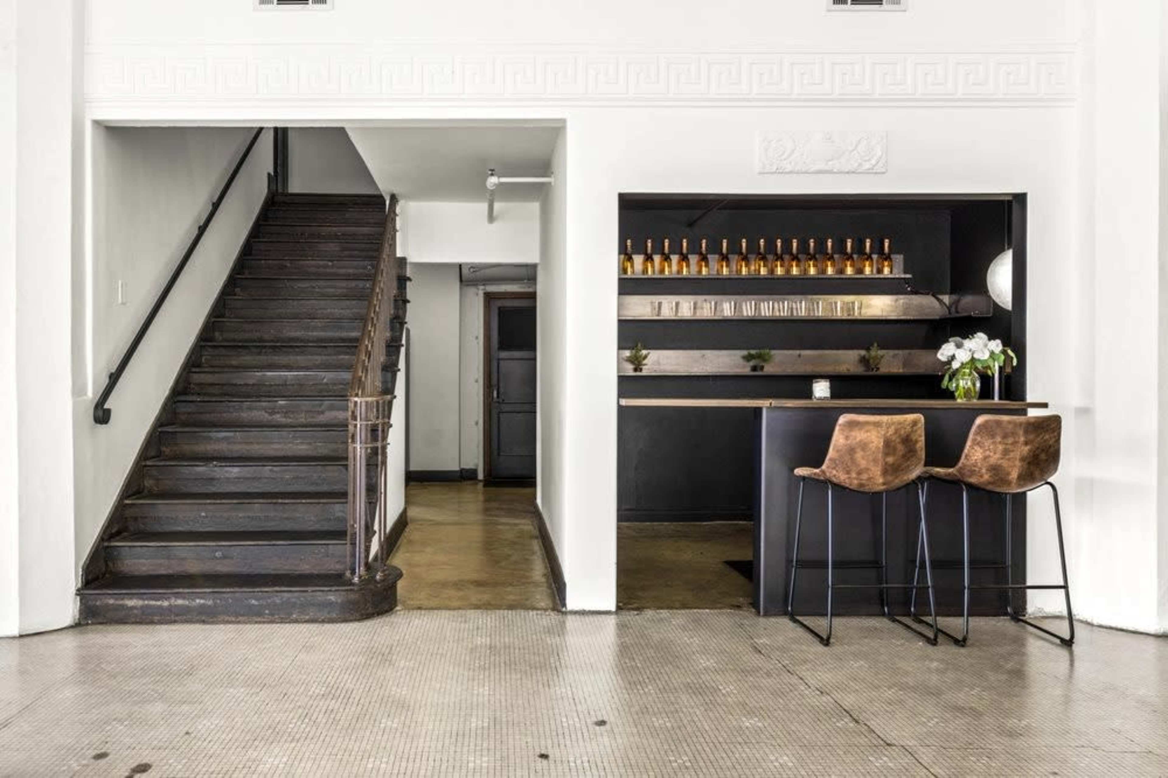 The image shows a modern interior featuring a staircase on the left and a sleek bar area with two stools on the right.