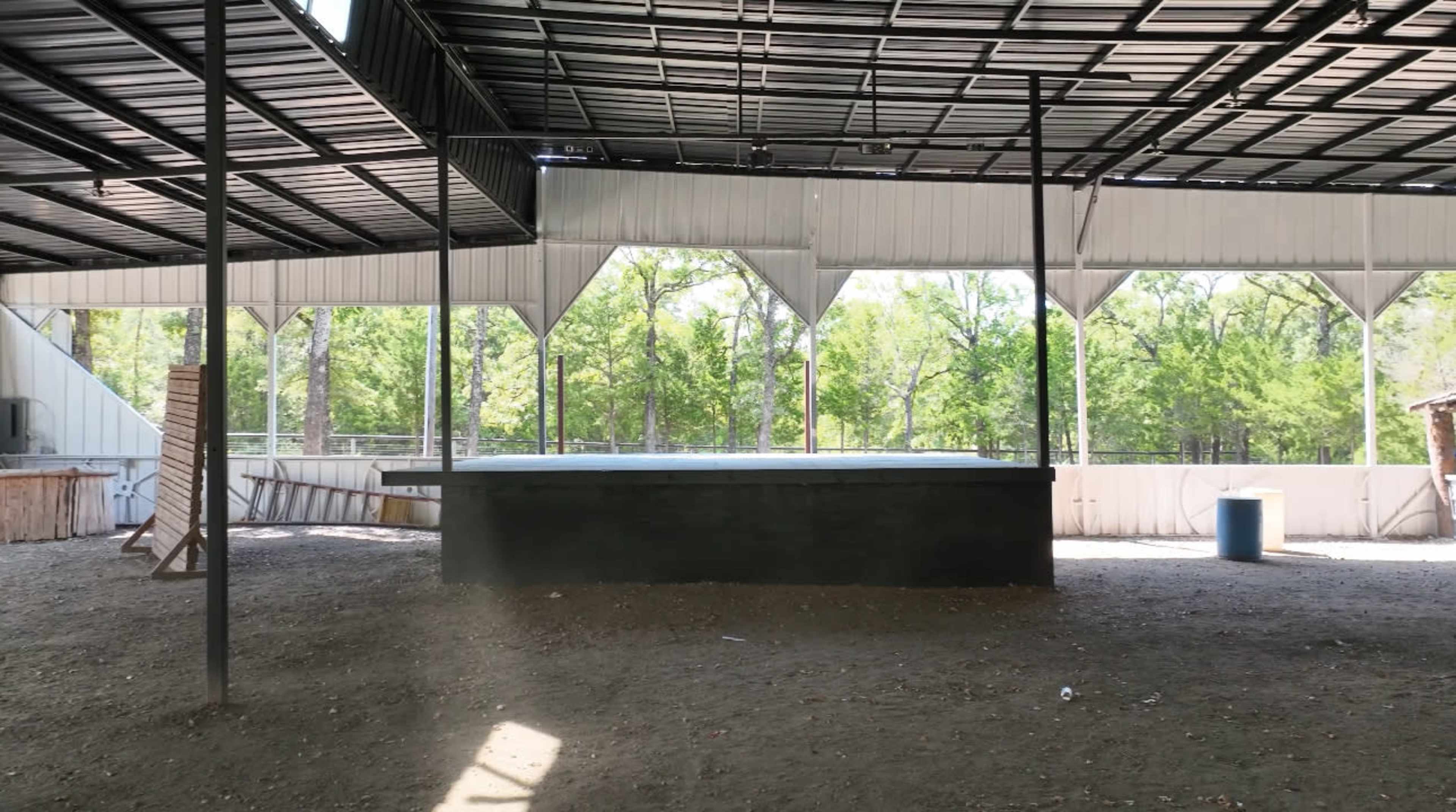 The image shows an open, covered area with a large, flat platform and trees visible in the background.