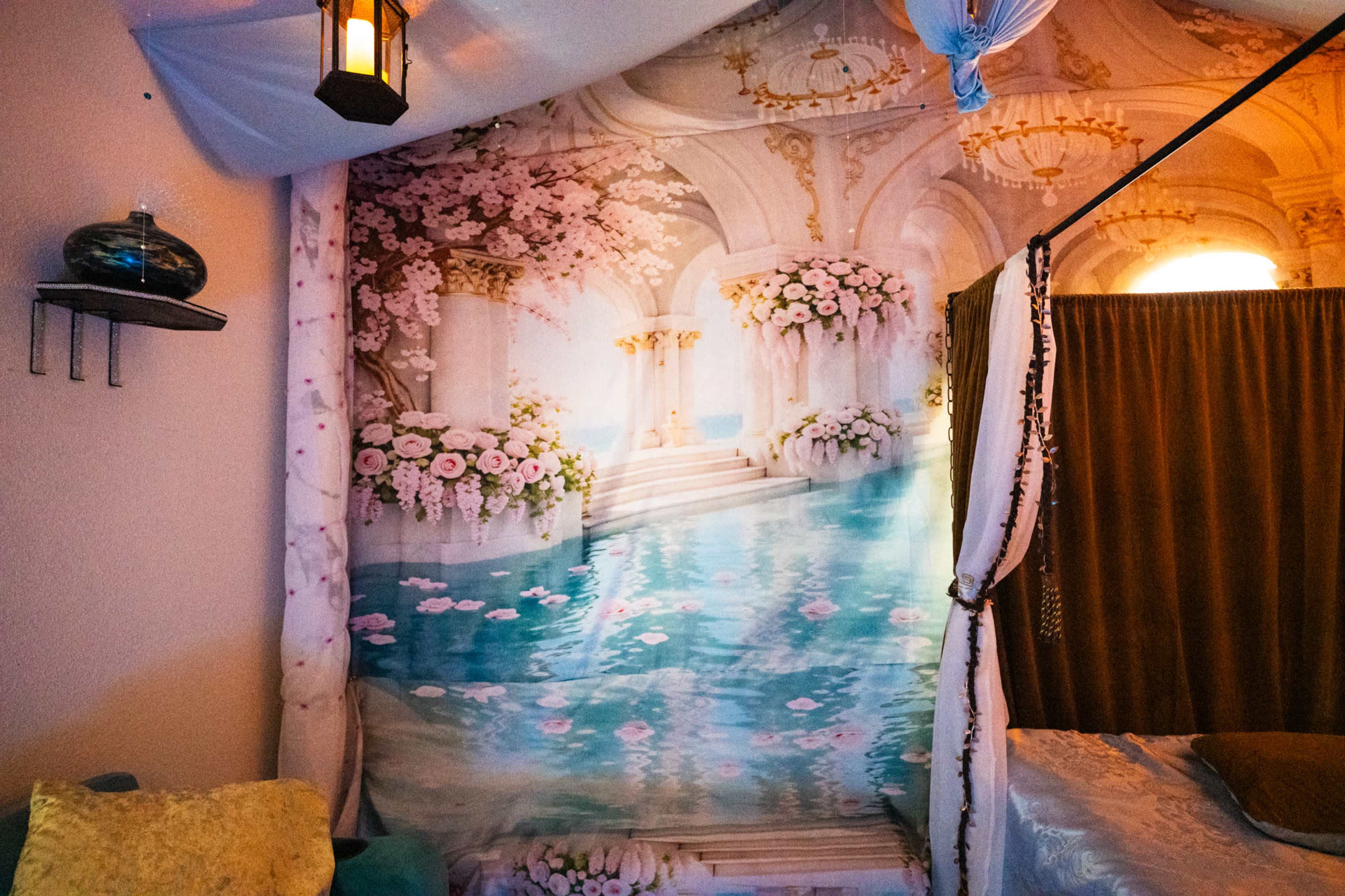 The image features a mural depicting a tranquil scene with a pool and ornate architecture, adorned with pink flowers.