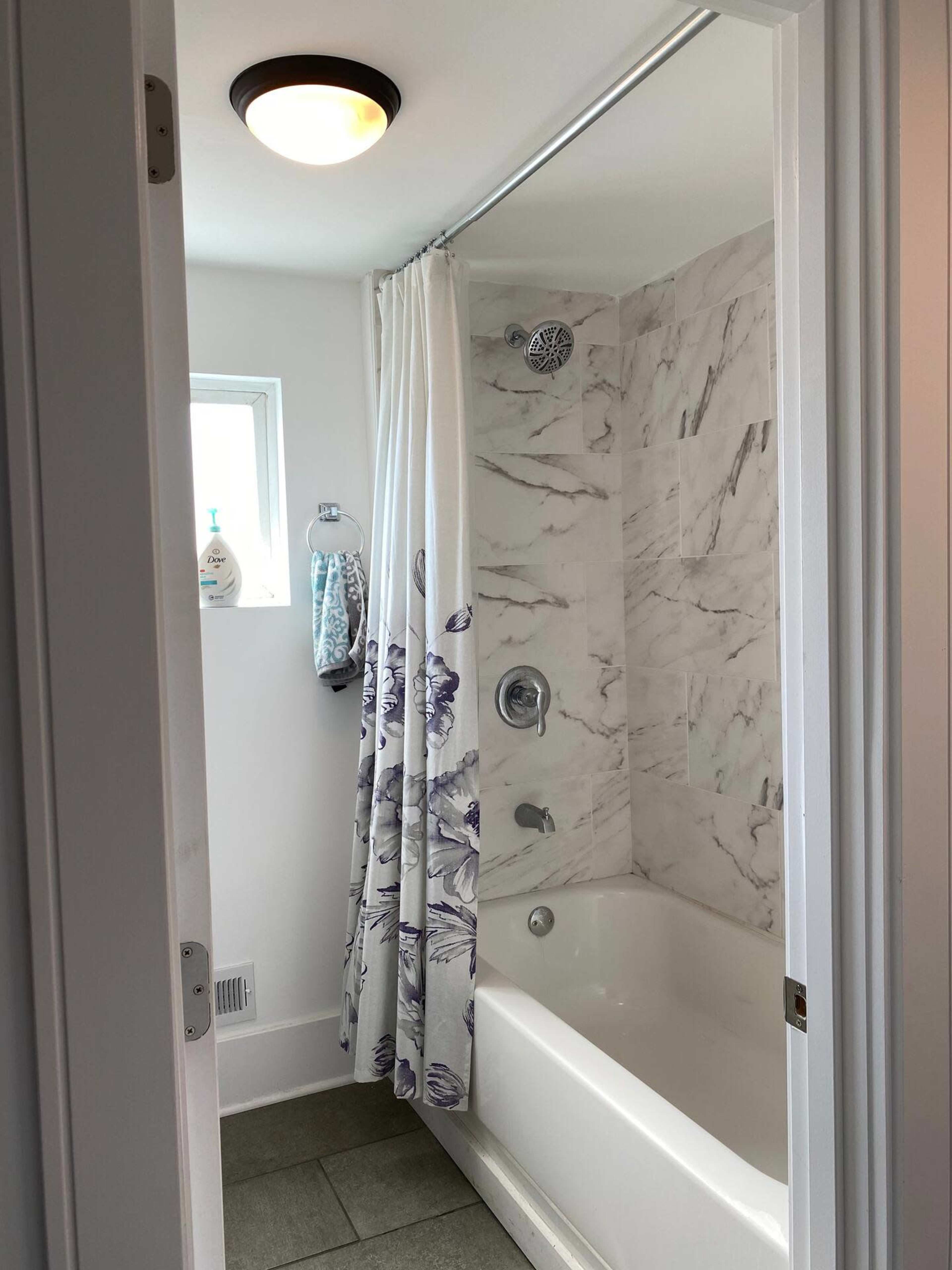 A bathroom features a bathtub with a shower curtain, marble walls, and a small window.