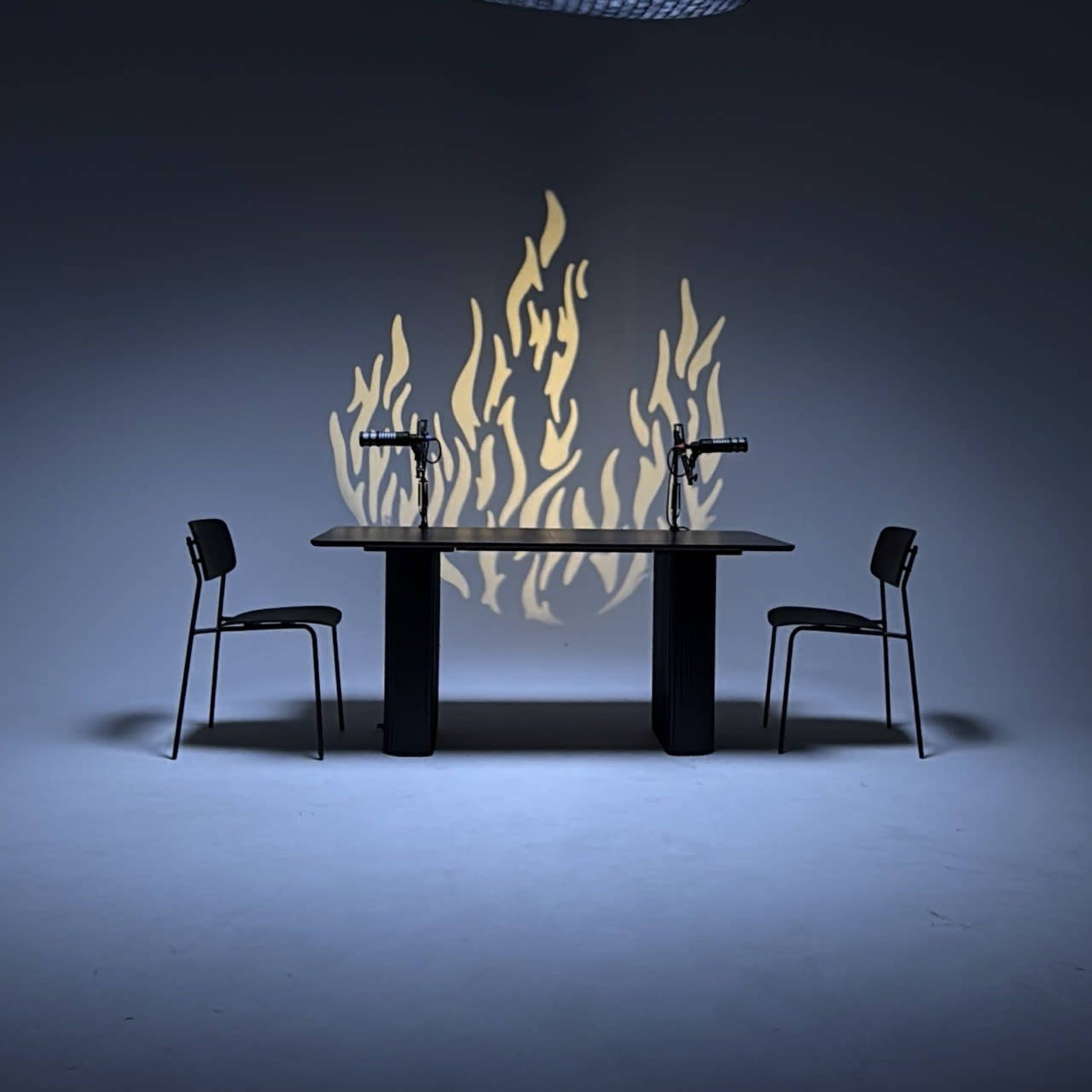A dark room features a table with two chairs, and shadows of flames are projected on the wall behind it.