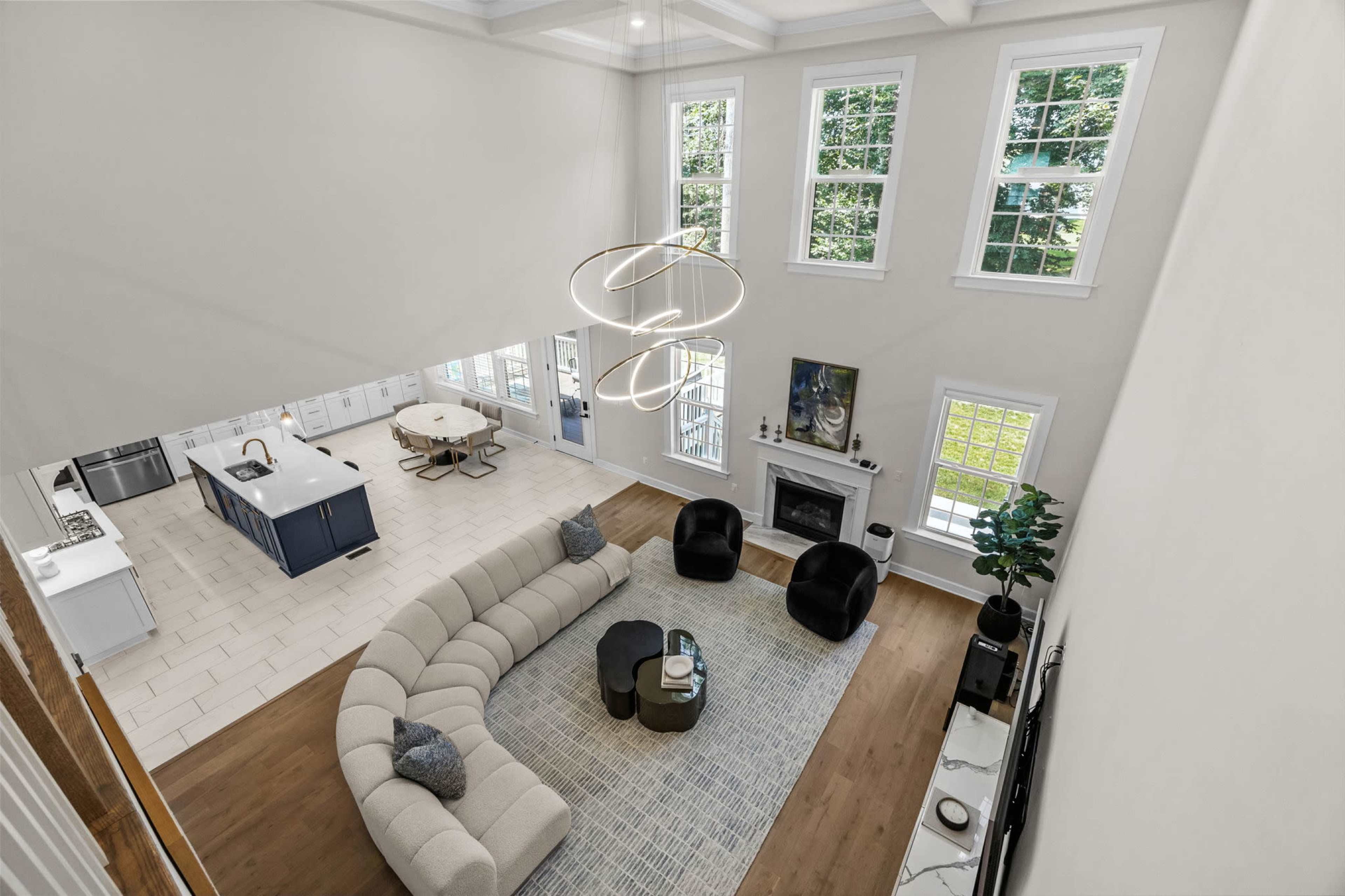A spacious modern living room features a curved sectional sofa, two black armchairs, a round coffee table, and large windows that allow natural light to fill the space.