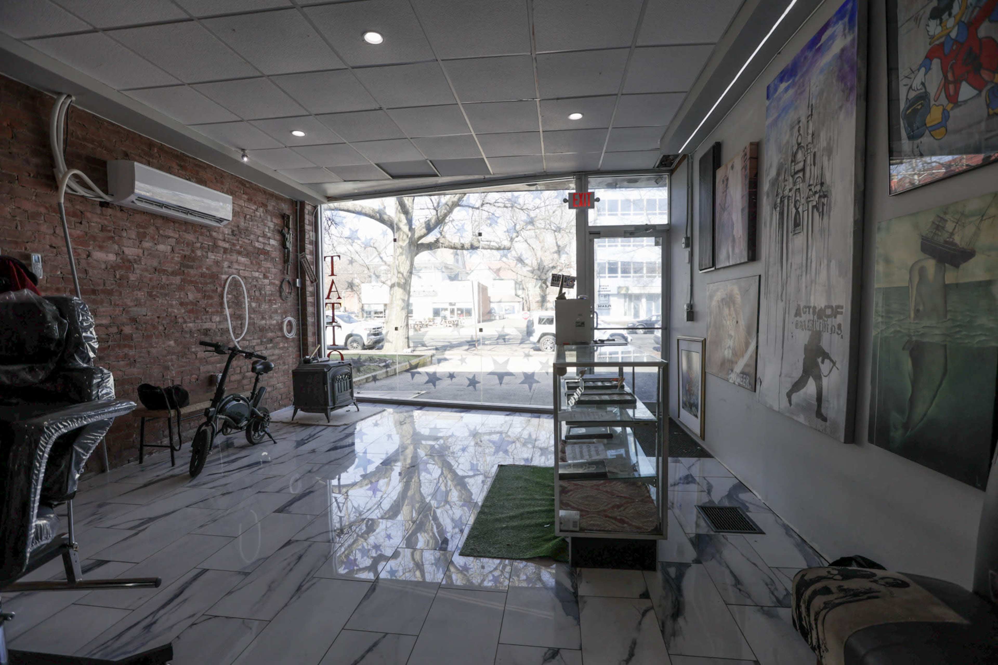 A spacious tattoo parlor with large windows, polished marble floors, and artwork displayed on the walls.