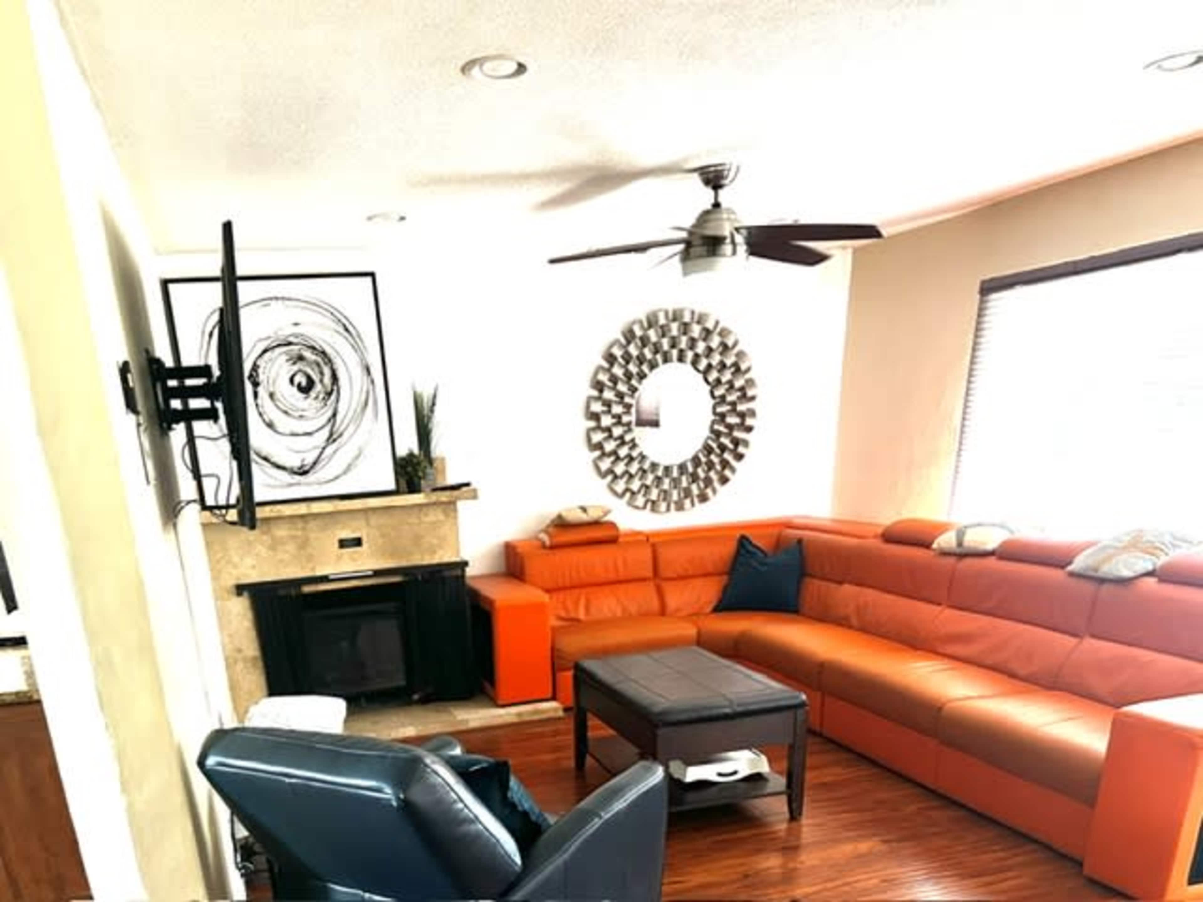 The living room features an orange sectional sofa, a mounted television, and a circular wall mirror above a stone fireplace.