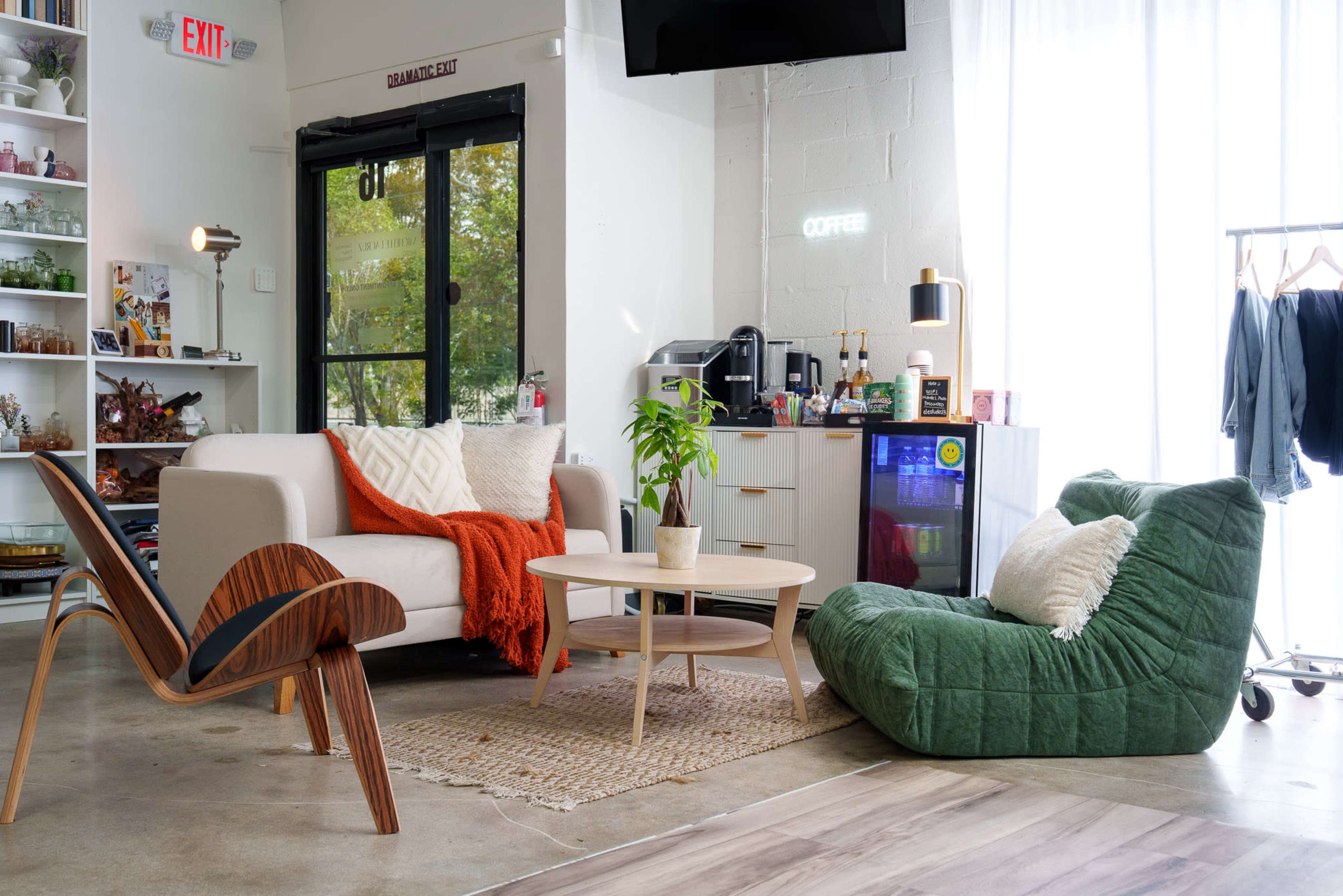 The image shows a modern, cozy interior featuring a light-colored sofa with an orange throw, a circular wooden coffee table, and two distinct seating options—a wooden chair and a green bean bag.